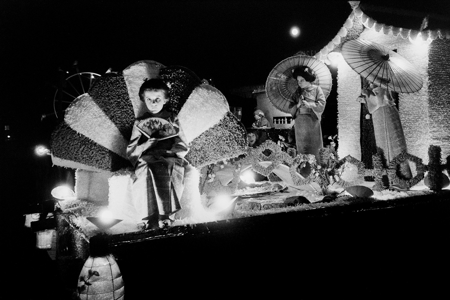 Women and a child on a Japanese themed carnival float at Hatherleigh Carnival, at night.