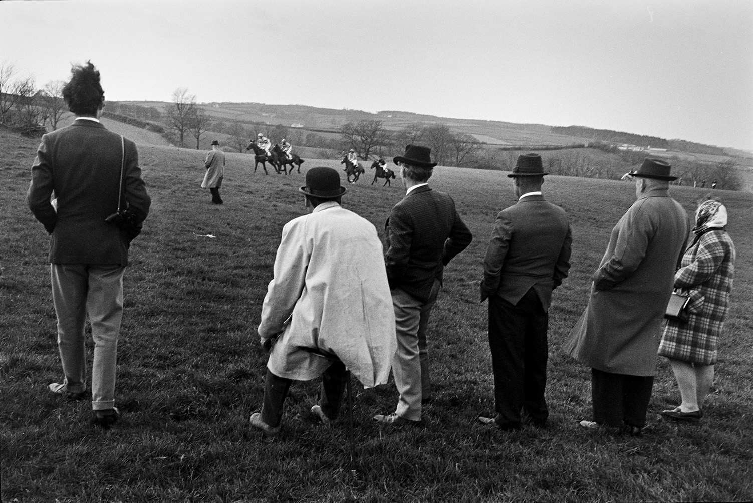 Spectators watching the Torrington Farmers Hunt Point to Point at Chapelton. The horses and riders can be seen competing in the field.