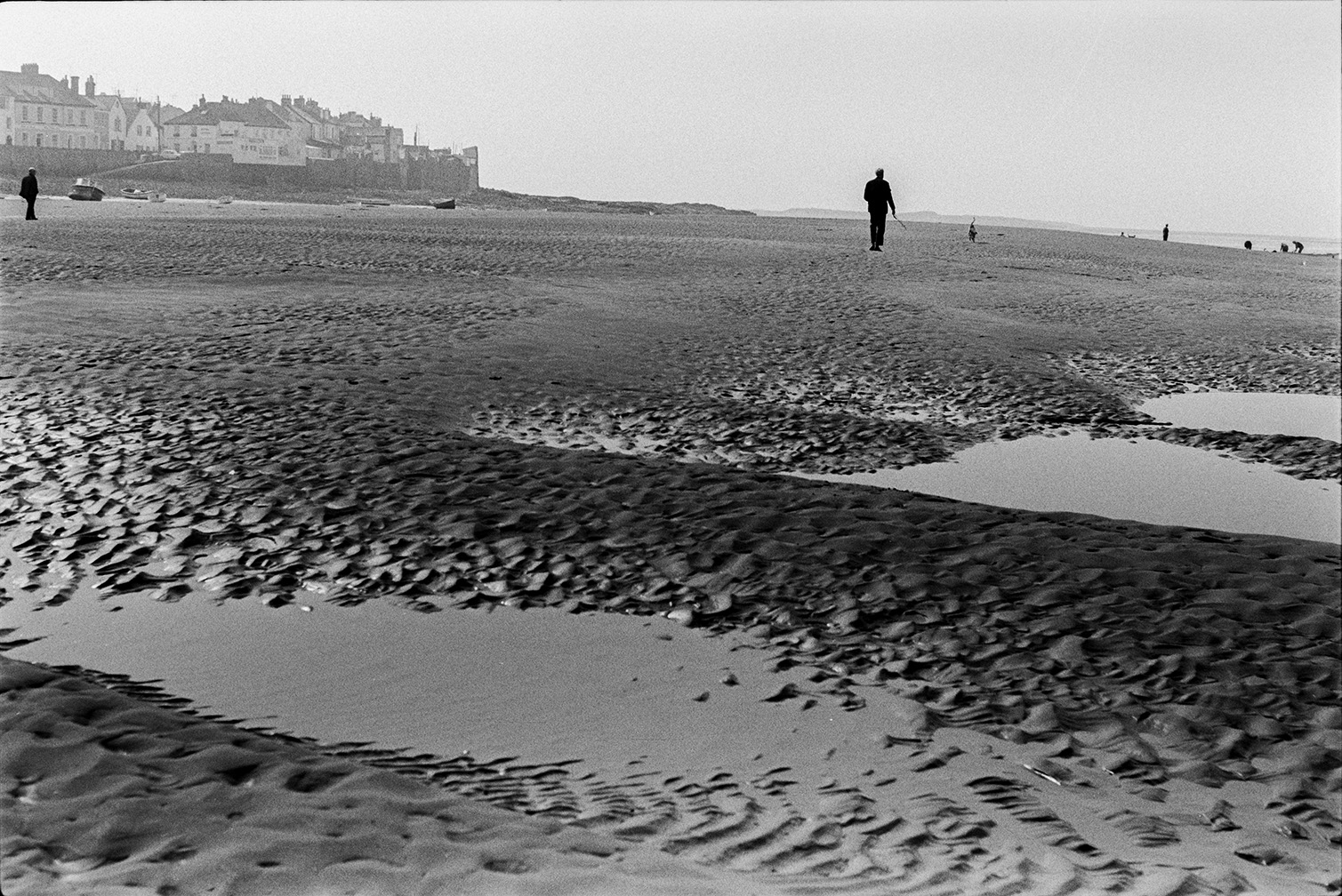 People walking along the beach after the tide has gone out at Appledore. The town can be seen in the background.
