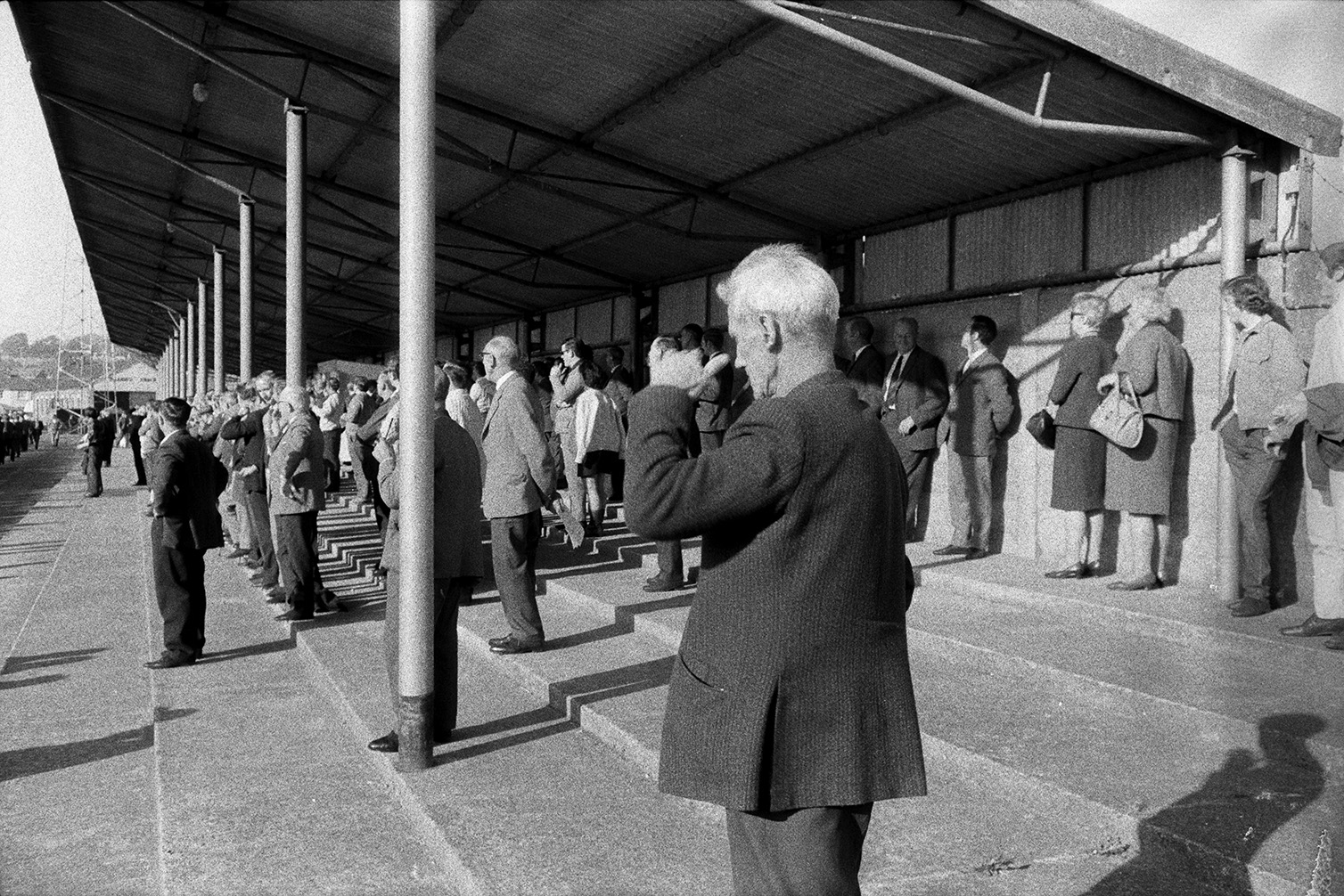 Men and women standing under a shelter and watching a parade or football match, possibly at Bideford.