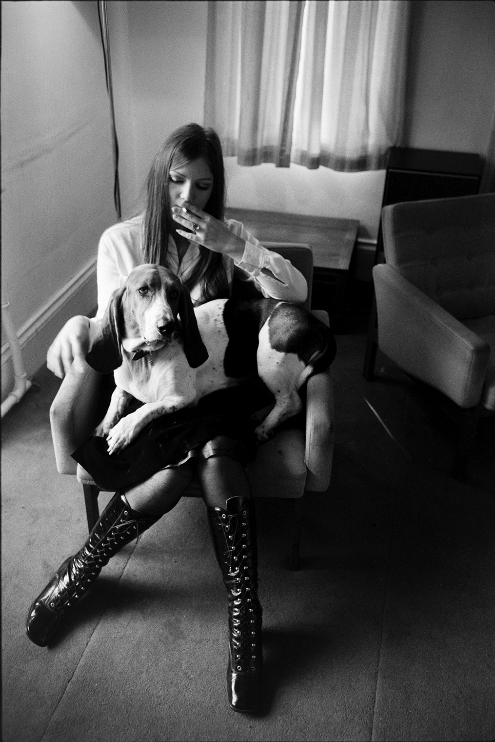 A young woman sat on a chair and smoking, possibly at the Beaford Centre. A Basset dog is sat on her lap.