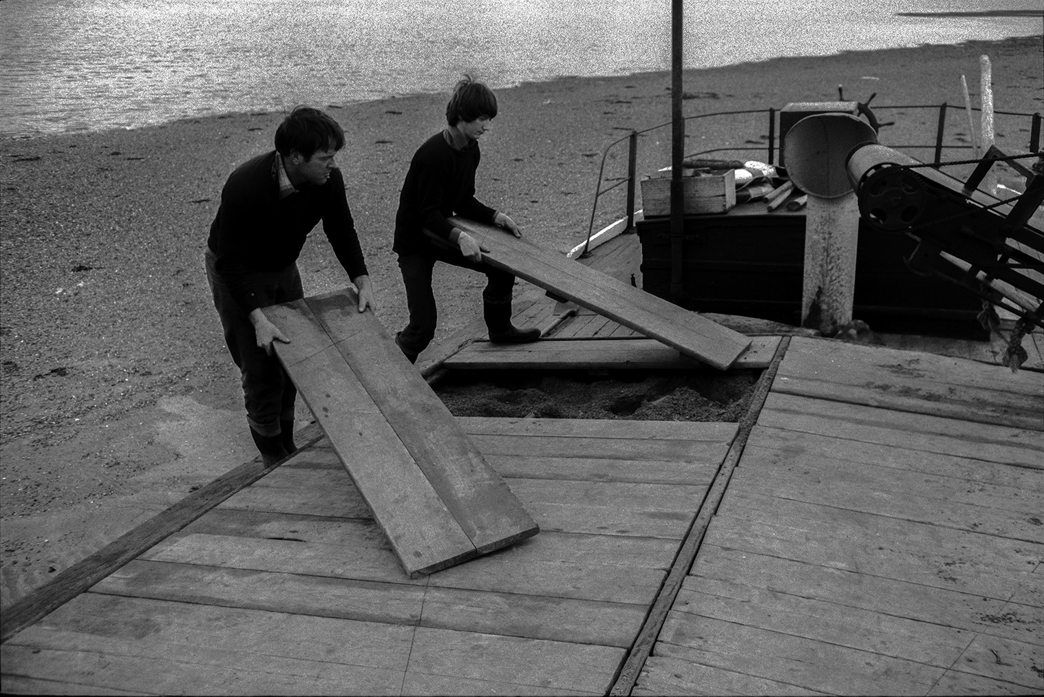 Two men covering a full sand barge with wooden planks on the beach at Crow Point, Braunton. The man on the left may be John Daniel.