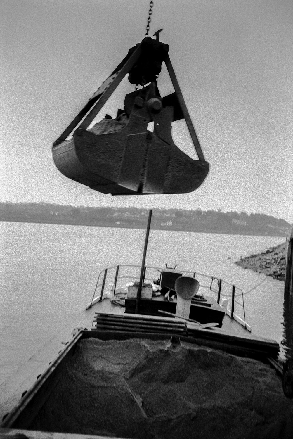 The mechanical grab of a crane unloading sand from a barge onto a dockside, possibly on the Taw River estuary.