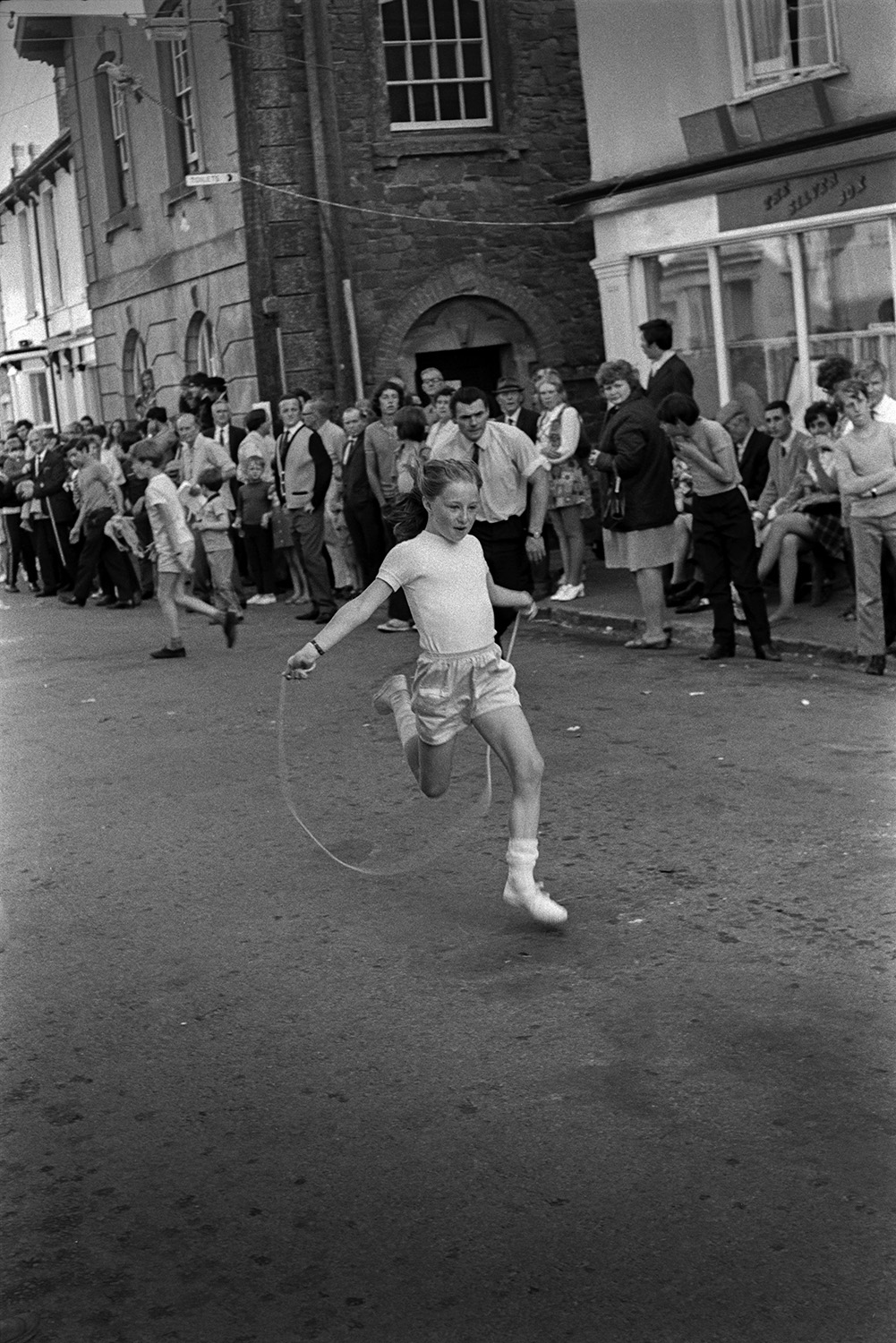 A girl competing in a skipping race through  a street at Chulmleigh Fair with spectators watching.