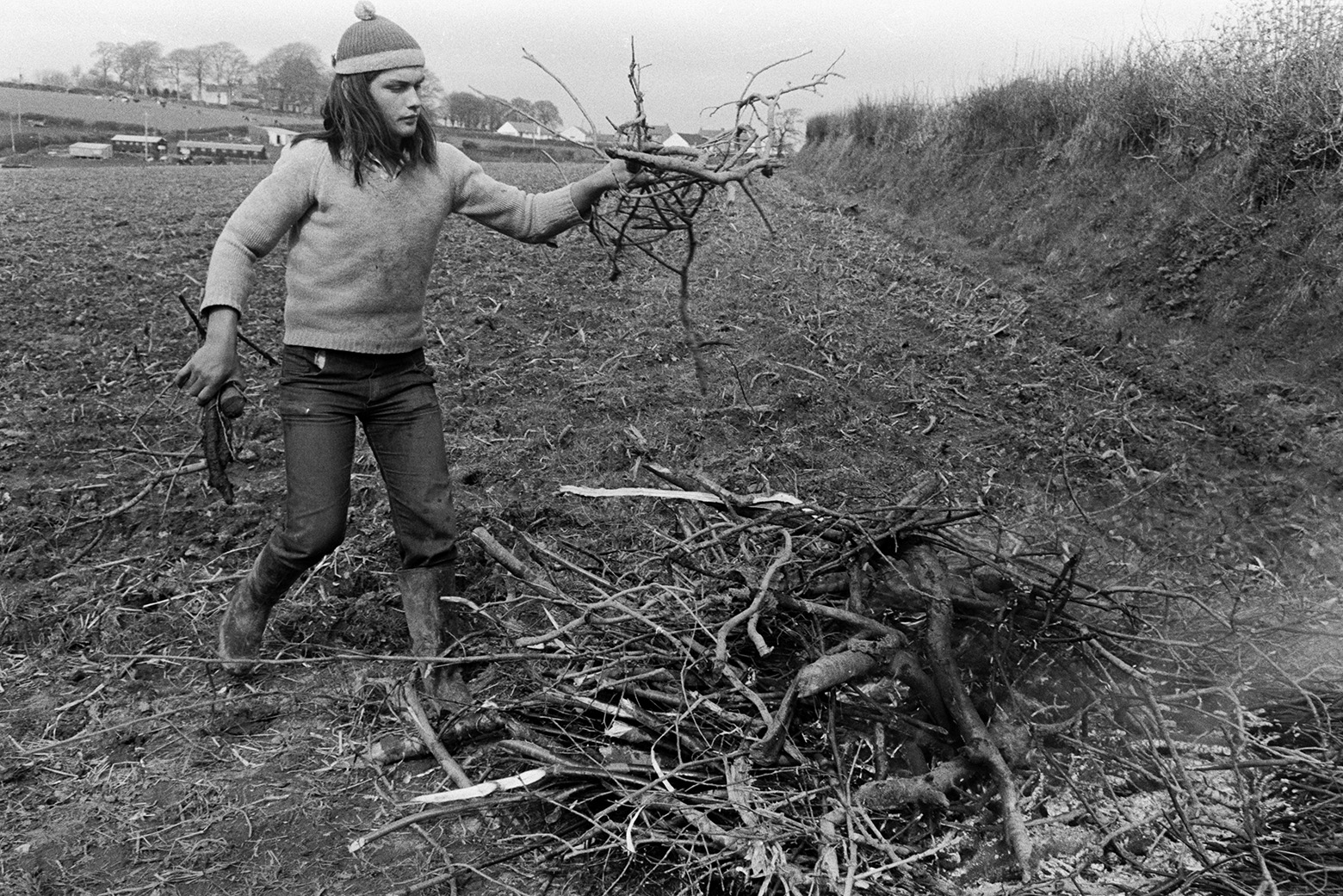 Derek Bright clearing sticks and twigs from a field at Mill Road Farm, Beaford, to make it ready to plant corn. He is building a small bonfire with the sticks. The farm was also known as Jeffrys.
