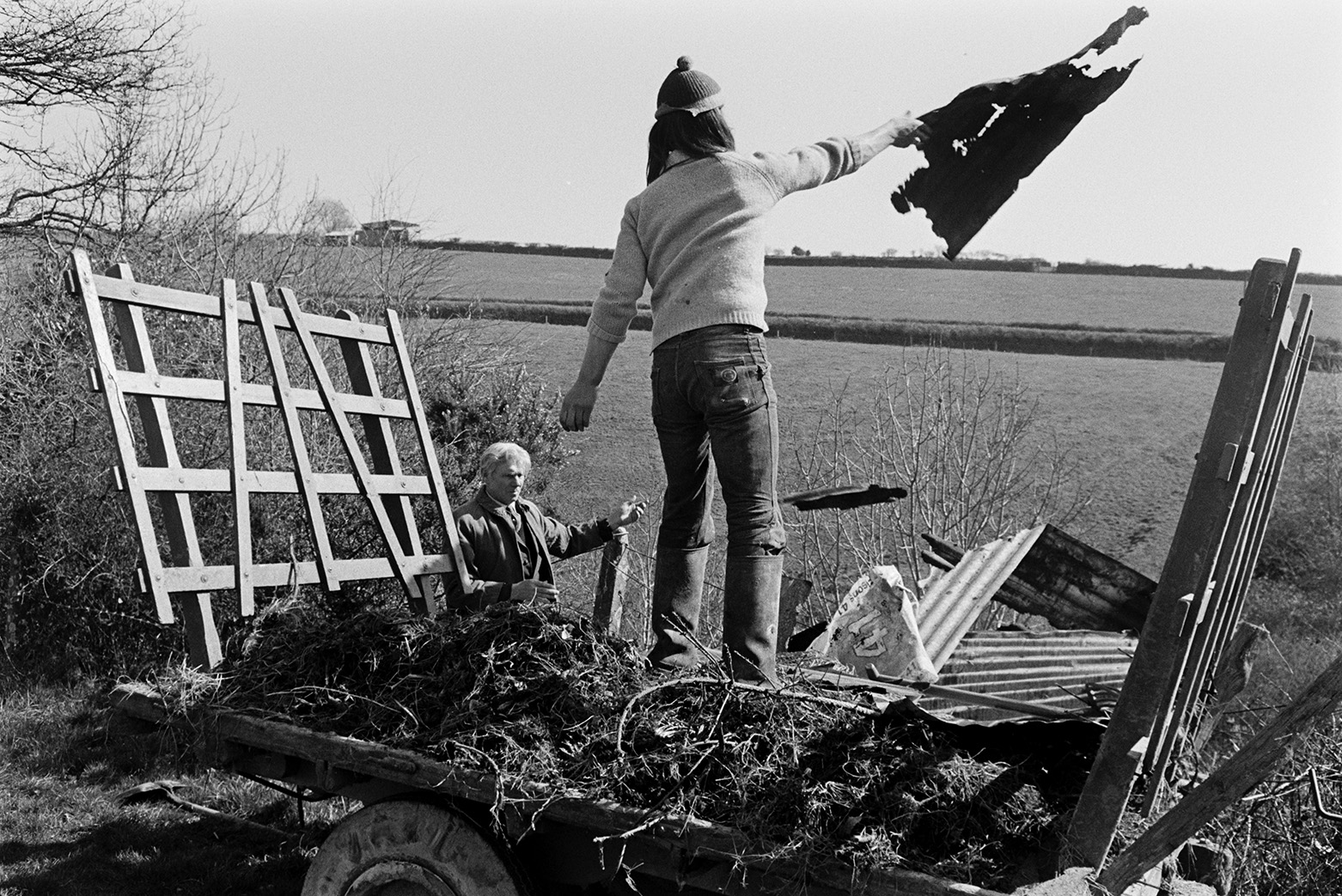 Derek Bright and Ivor Bourne dumping old corrugated iron sheets and brambles from a trailer by a hedge in Beaford.
