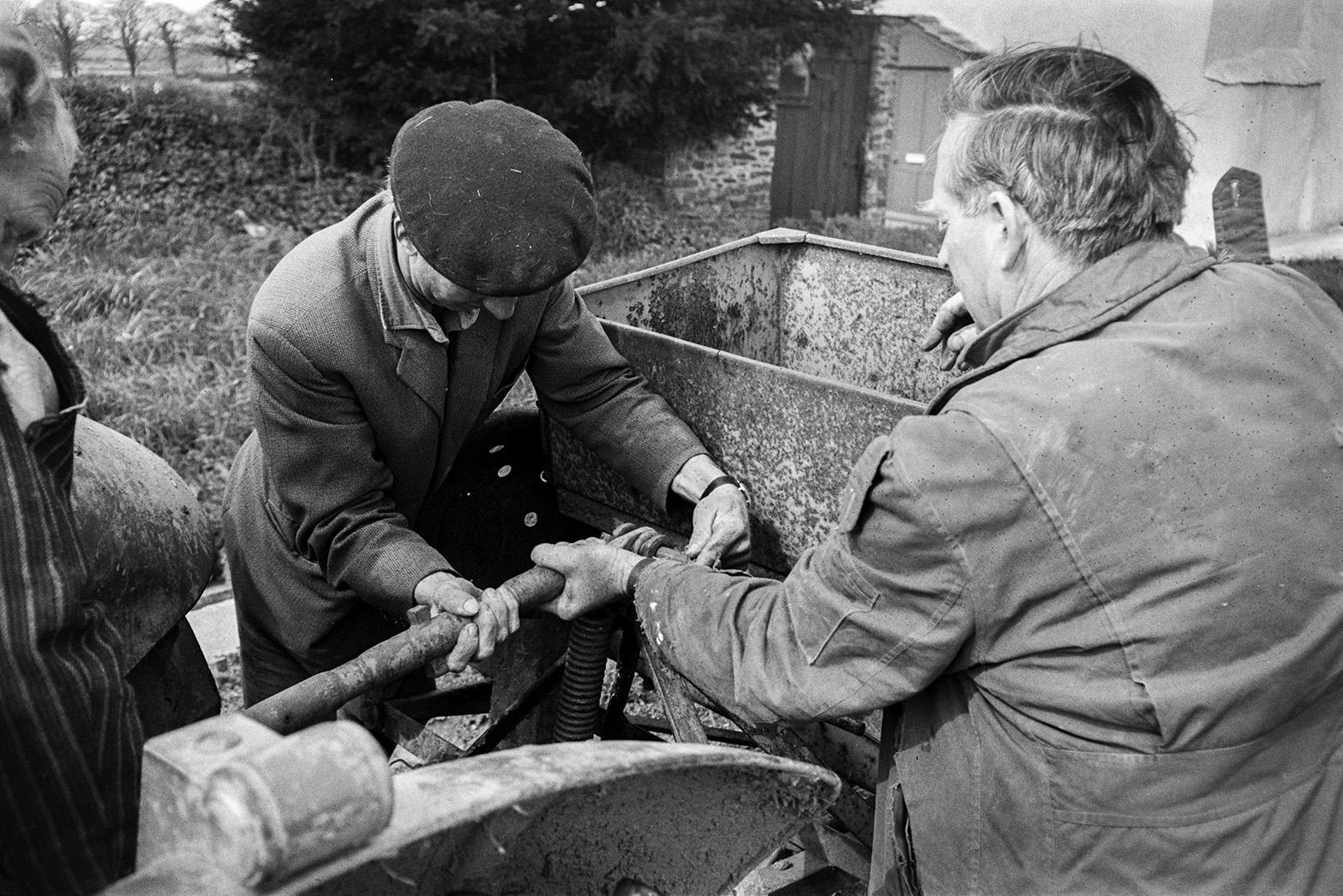 Three men attaching a potato tiller to a tractor in a farmyard at Mill Road Farm, Beaford. Ivor Bourne is in the centre. The farm was also known as Jeffrys.