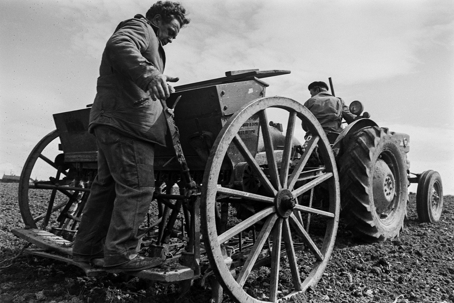 Men planting corn using a corn tiller in a field at Mill Road Farm, Beaford. Ivor Bourne is driving the tractor. The farm was also known as Jeffrys.