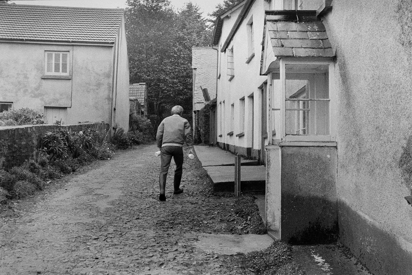 Ivor Bourne delivering milk bottles to a row of cottages along a lane in Beaford.