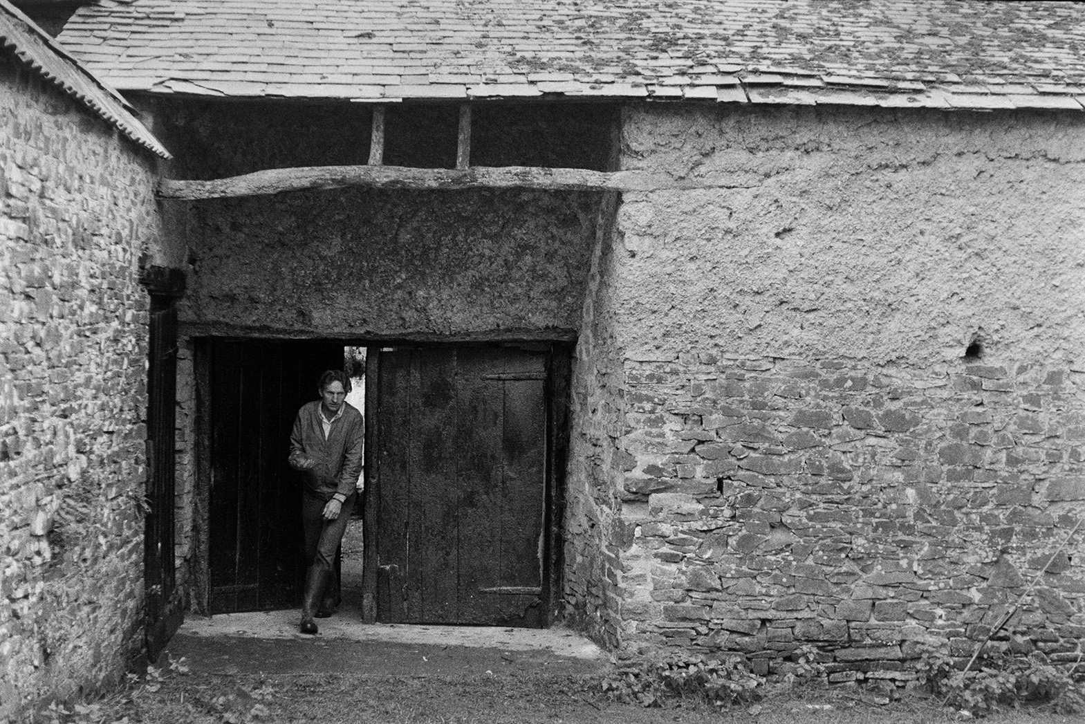 Ivor Bourne walking through wooden gates by a cob and stone barn in Beaford, possibly after his milk round.