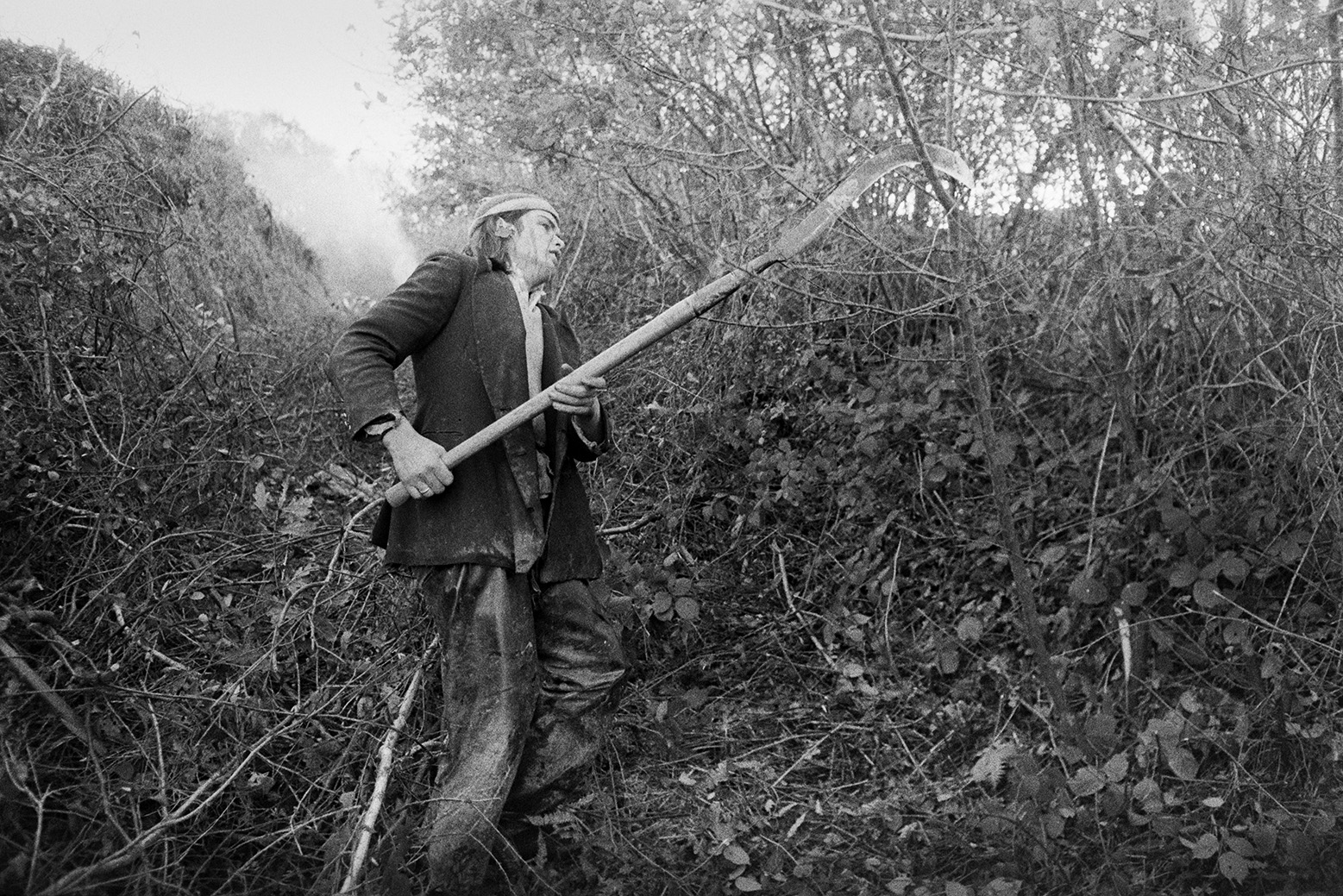 Derek Bright using a bill hook to trim hedges in Green Lane, Beaford. Smoke from the burnt cuttings can be seen in the background.