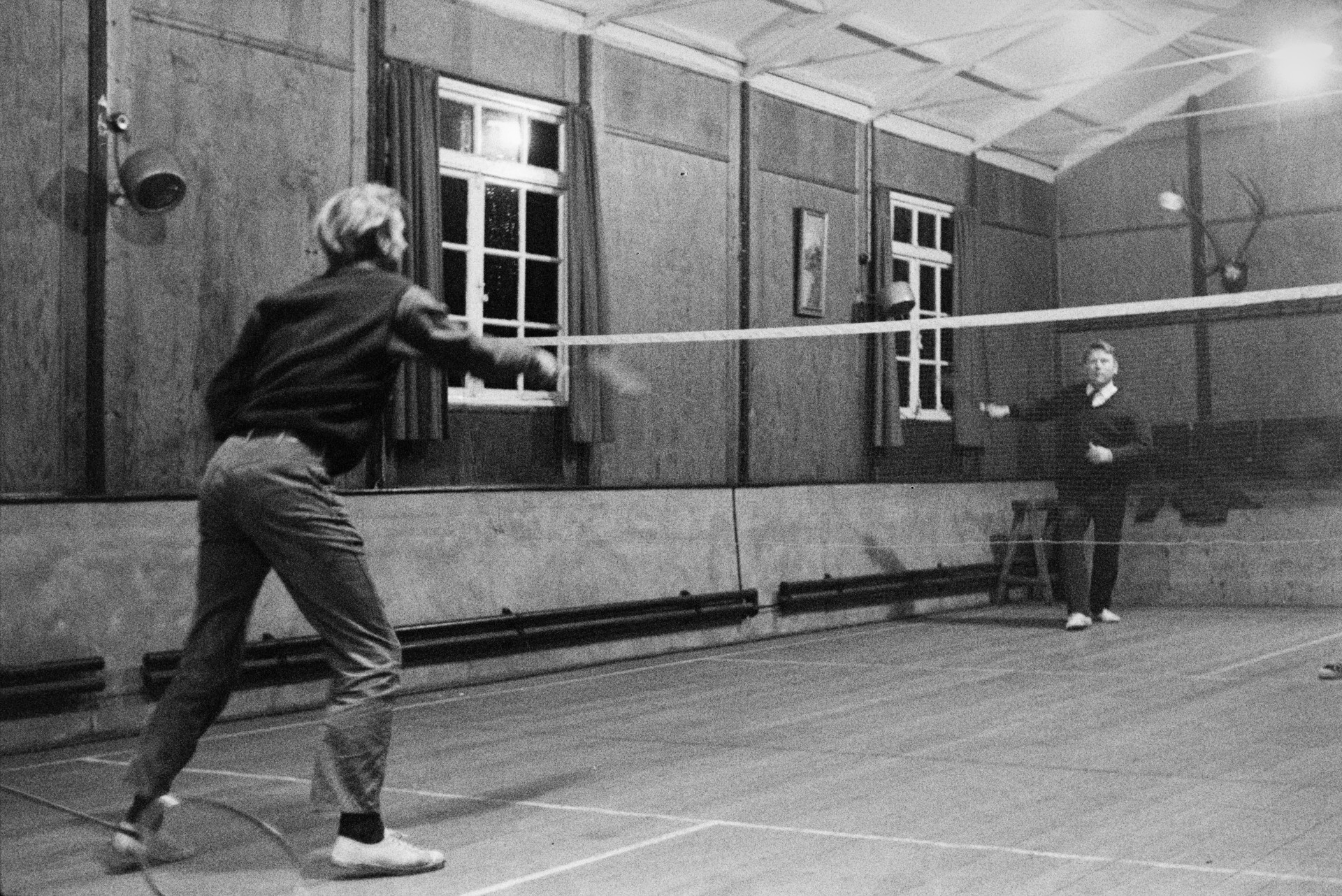 Two men playing badminton in a village hall. It is possibly a match between Bideford and Hatherleigh.
