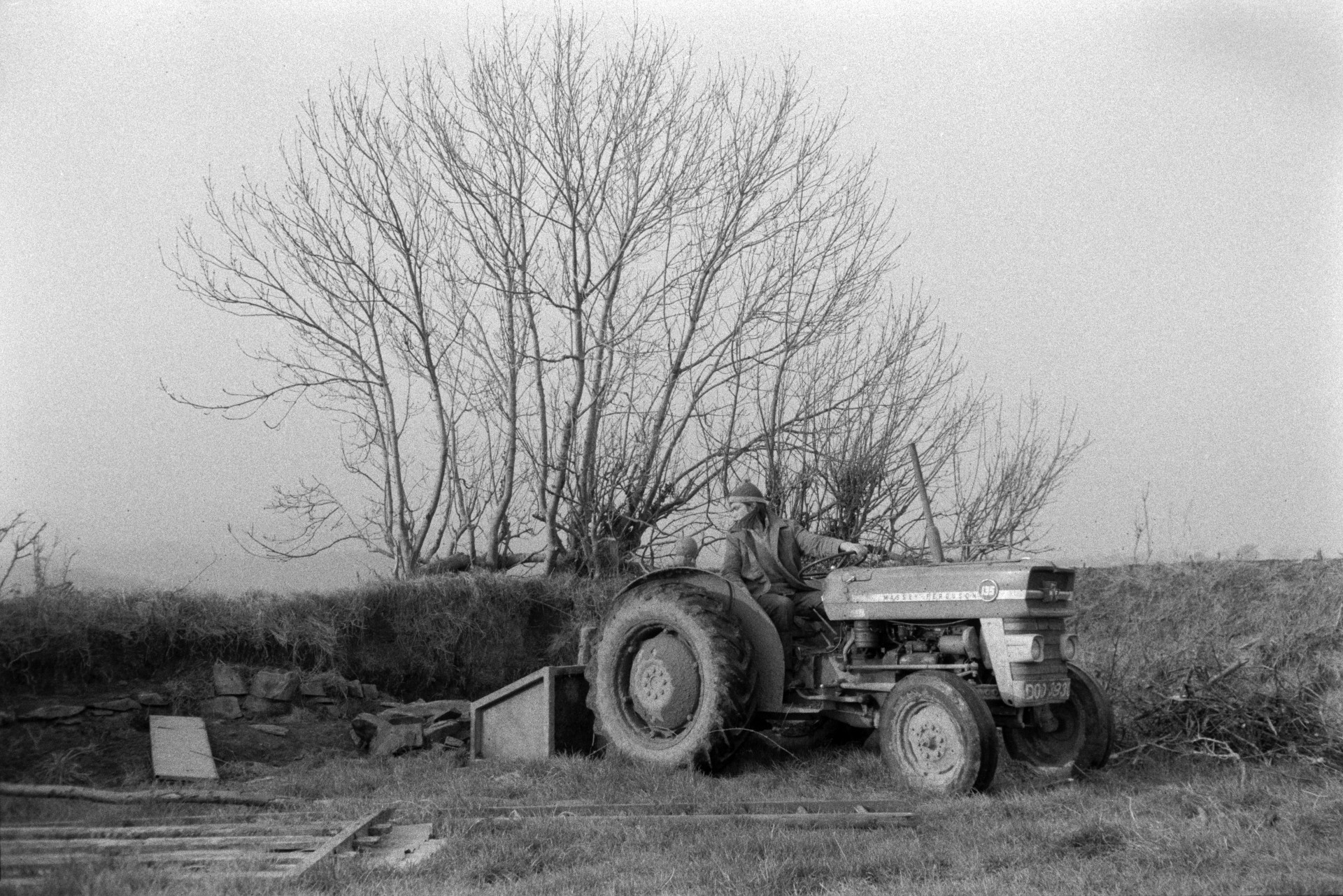 Derek Bright driving a tractor and link box loaded with stones to a hedge, in a field at Mill Road Farm, Beaford, so the stones can be used to strengthen the hedge. The farm was also known as Jeffrys.