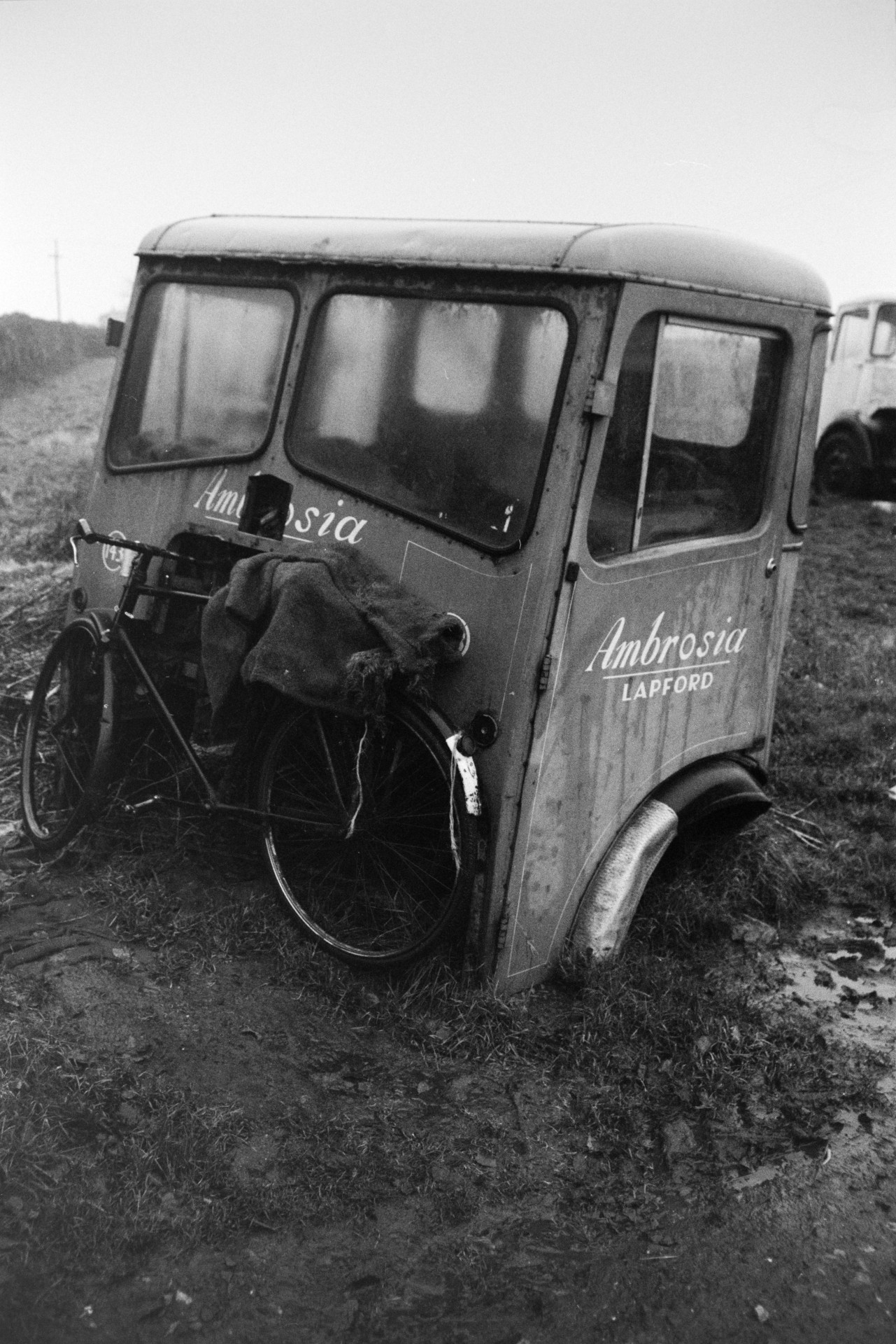 A bicycle propped next to an old stripped down Ambrosia lorry cab.