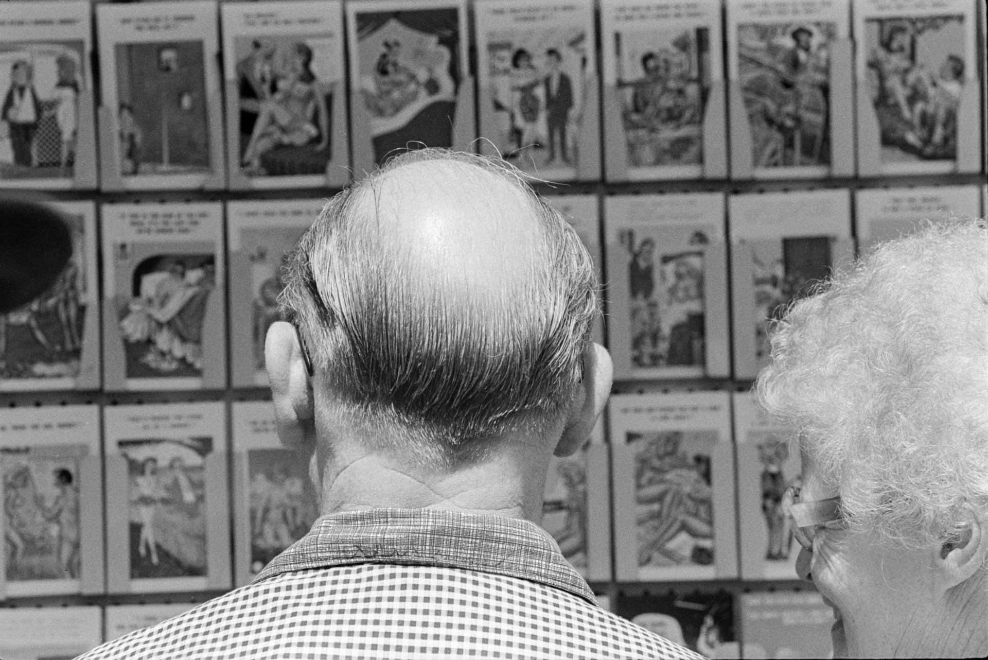 A man and woman looking at a postcard display in a shop window at Ilfracombe.