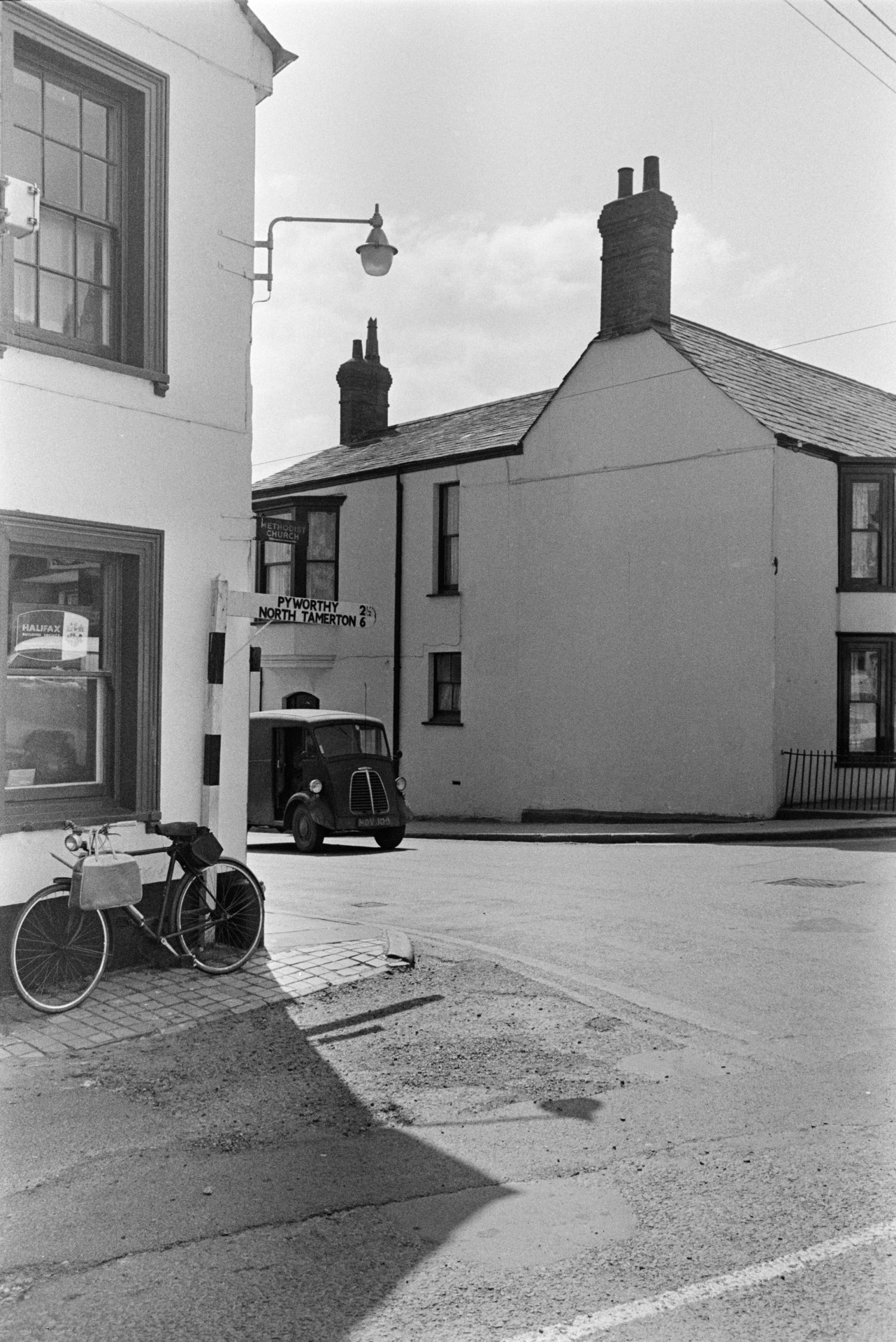 A street in Holsworthy with houses and a van. A bicycle is parked by a window, next to a signpost.