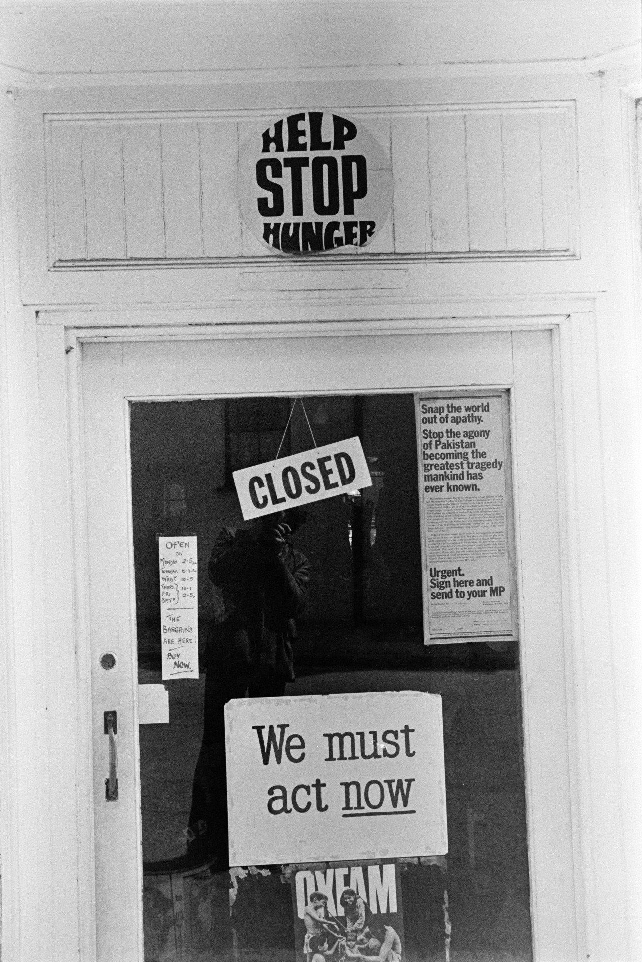 A shop door with a closed sign and posters in Holsworthy. A poster for Oxfam is stuck to the door.