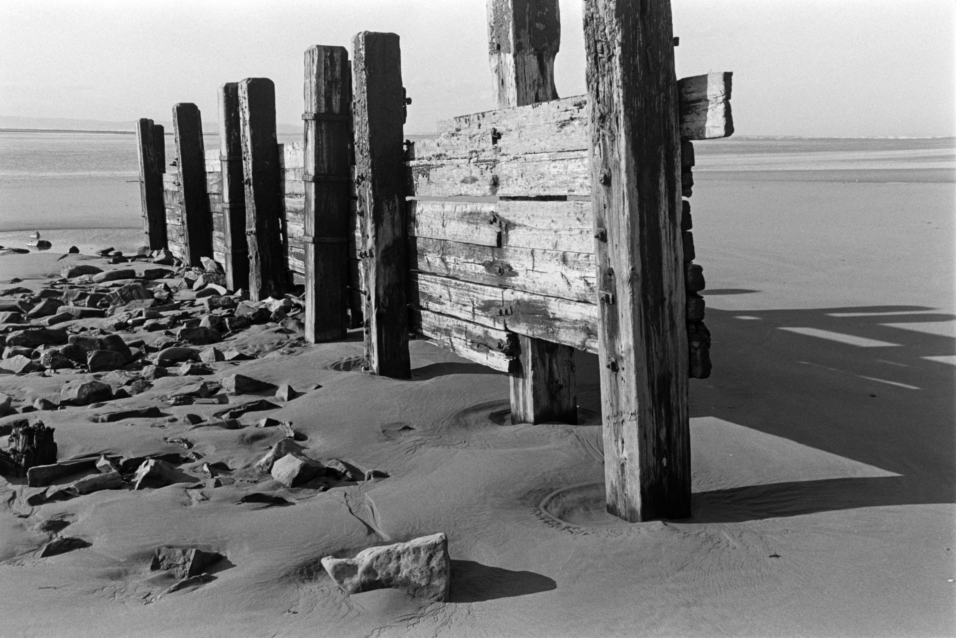 A wooden groyne on the beach at Saunton Sands. Small rocks have washed up against the groyne. The sea is visible in the background.