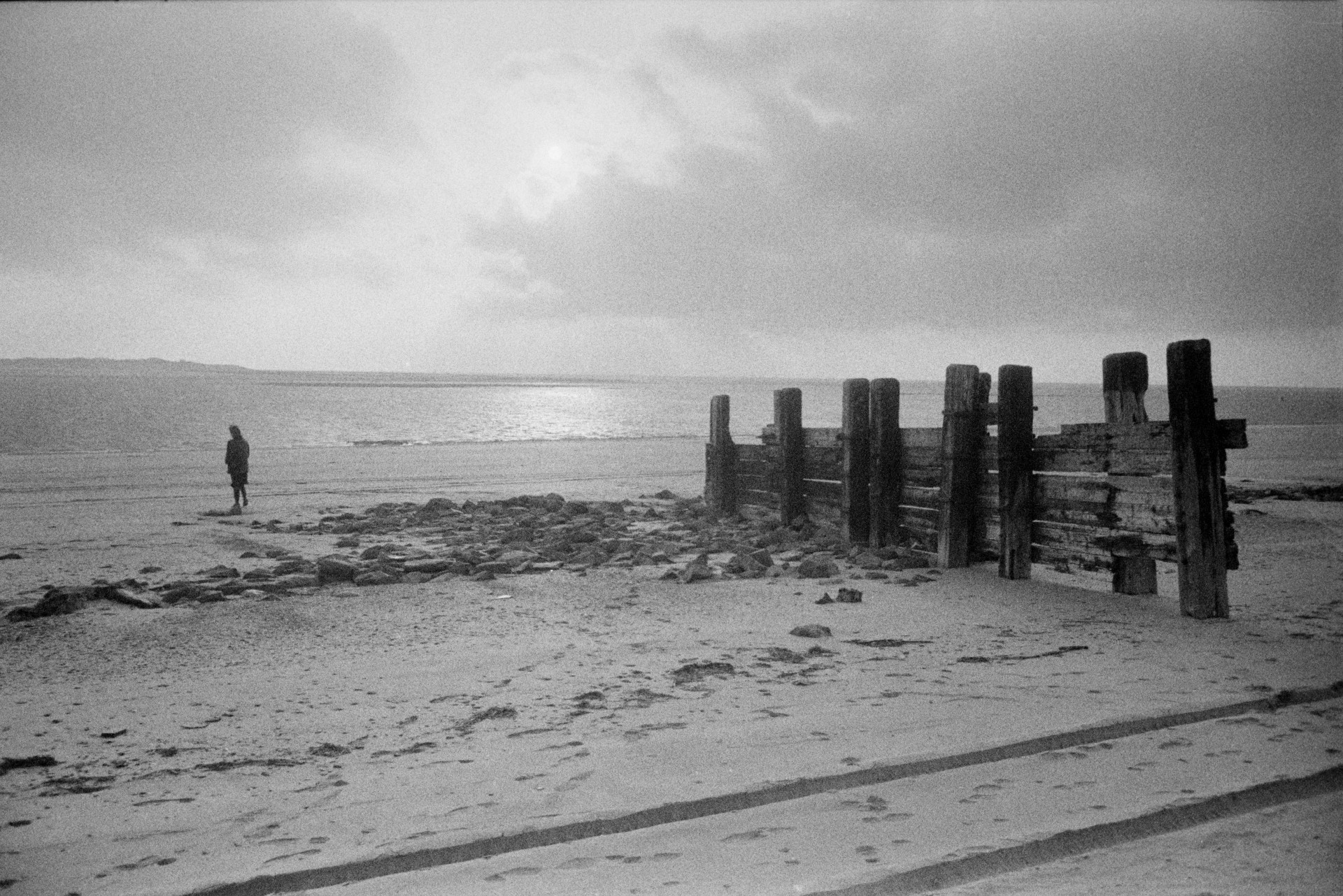 A person walking along the beach by a wooden groyne at Saunton Sands.