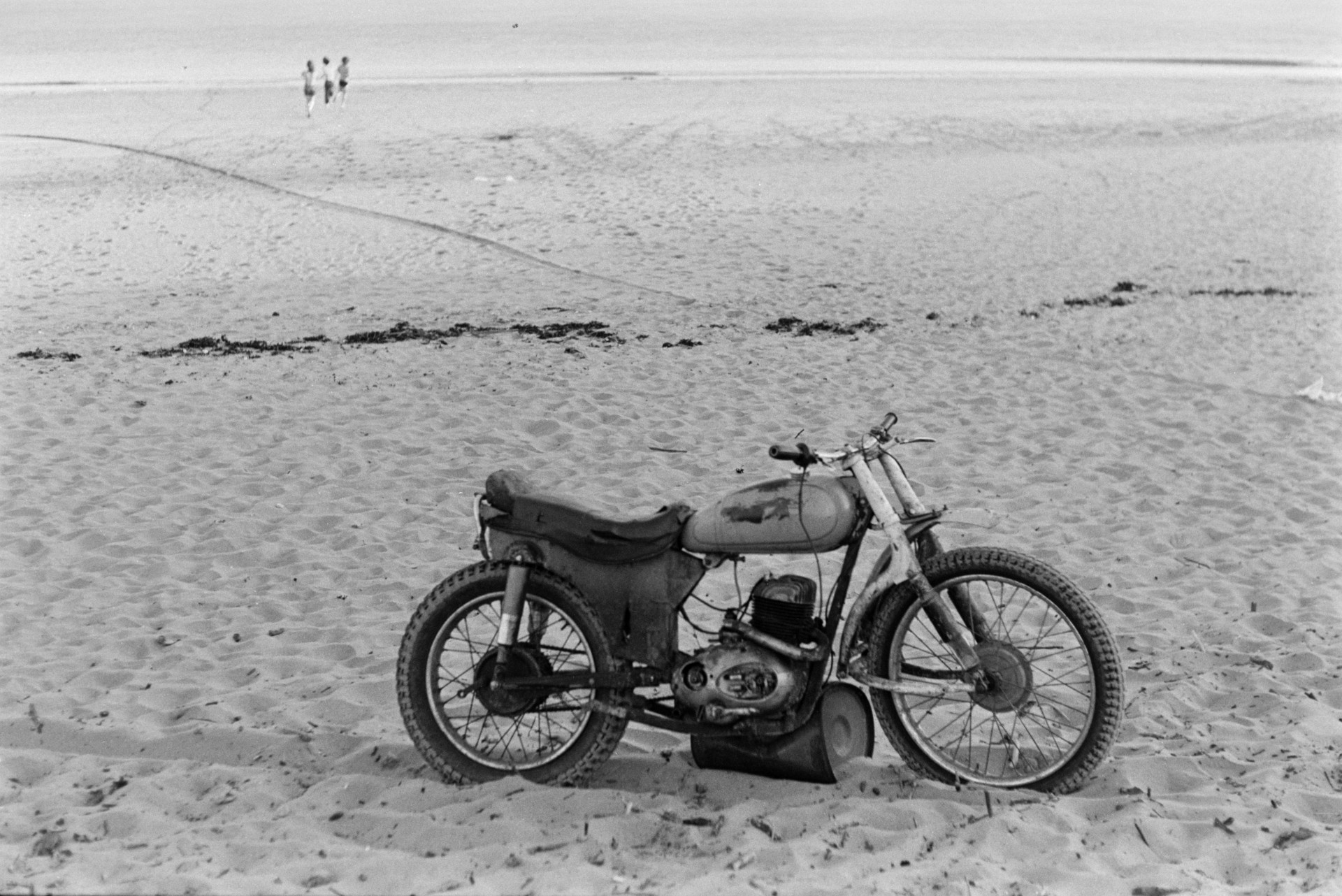 A motorcycle on the beach at Braunton with people running towards the sea in the distance.