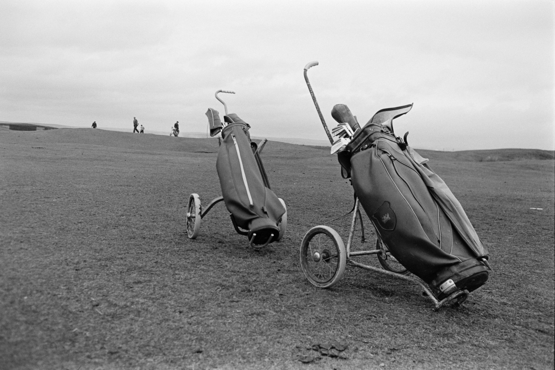 Golf bags and clubs on a golf course at Westward Ho! People can be seen playing golf in the distance.