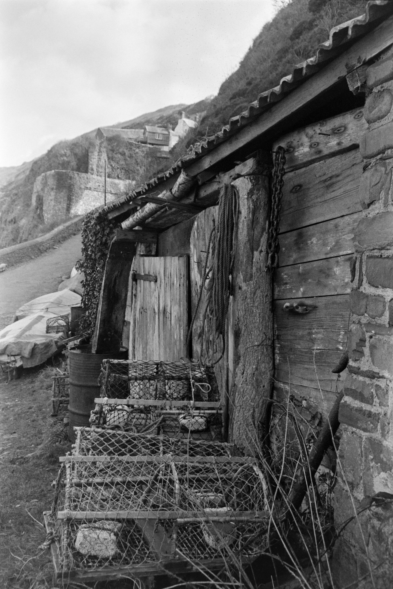 Lobster pots stacked in front of a shed with a tiled roof at Bucks Mills. Boats are hauled up next to a road by the shed.