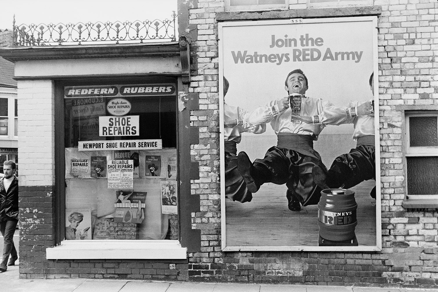 An advertising board on the outside wall of a shoe repair shop in Barnstaple. The board is advertising Watneys beer and reads 'Join the Watneys RED Army'.
