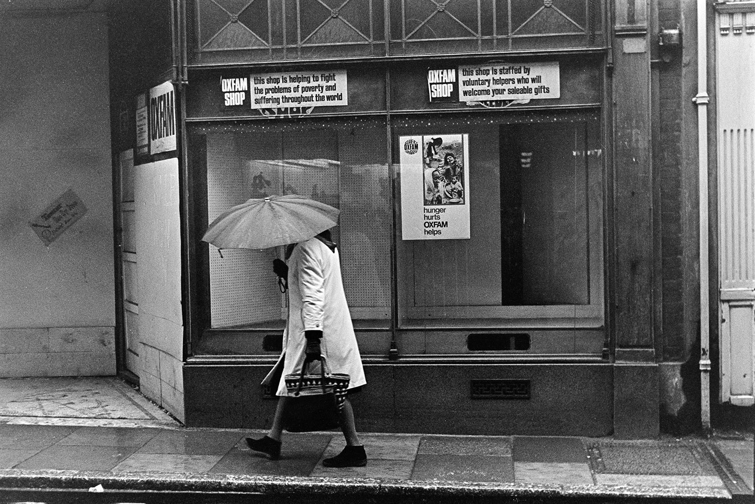 A woman holding an umbrella walking past an Oxfam shop front window in Barnstaple.