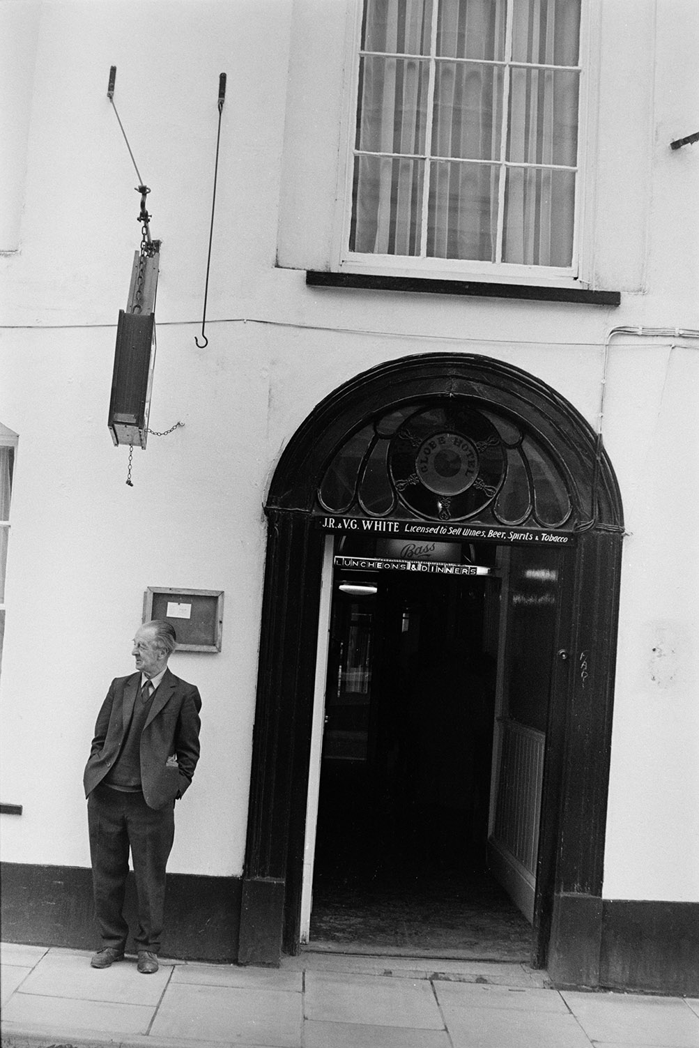 Man stood outside the entrance to the Globe Hotel. JR and VG White are the named licensees on the sign above the door.