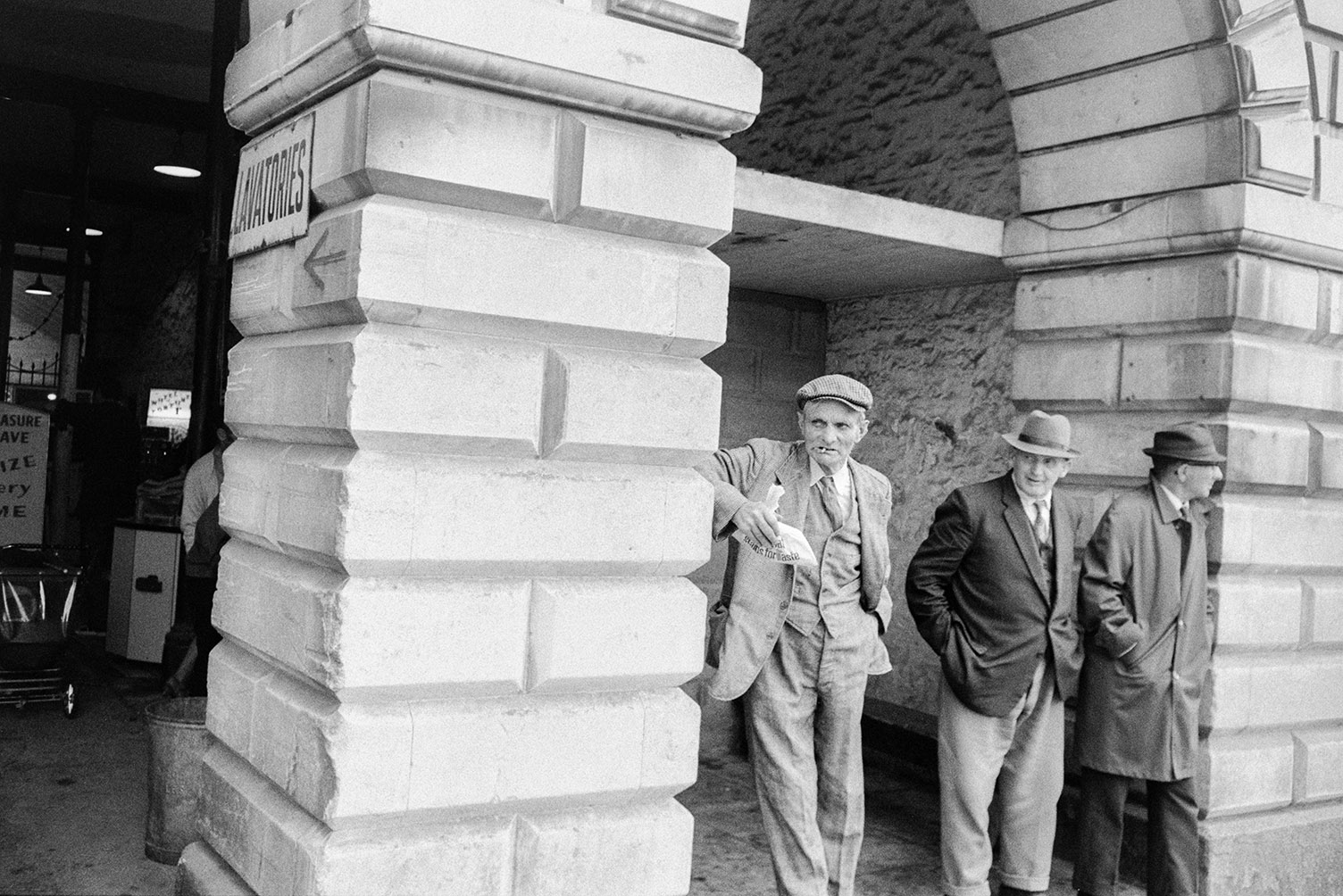 Three men stood under a stone arch of the Town Hall in South Molton, possibly watching the carnival parade.