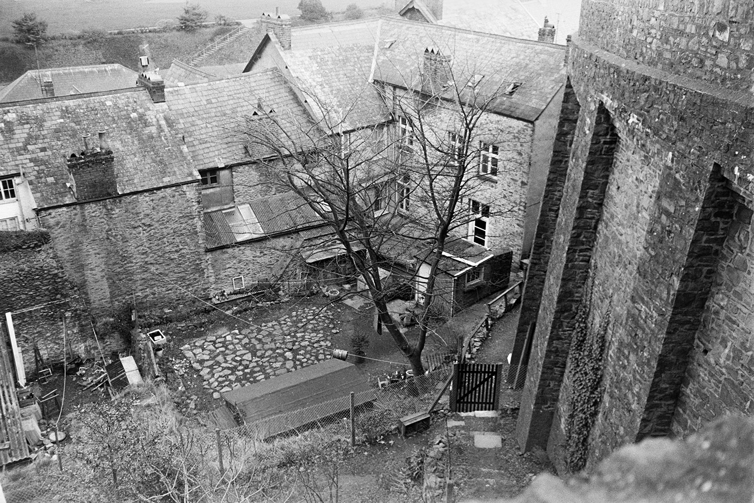 The back yard of houses in Lynmouth with sheds and a cobbled patio. The image is taken from a stone bridge or structure above the houses.