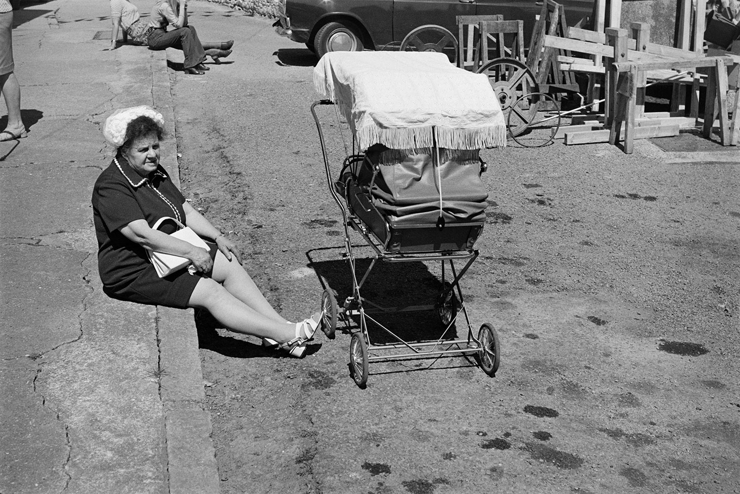 A woman sat on a pavement by a pram at Winkleigh Fair.