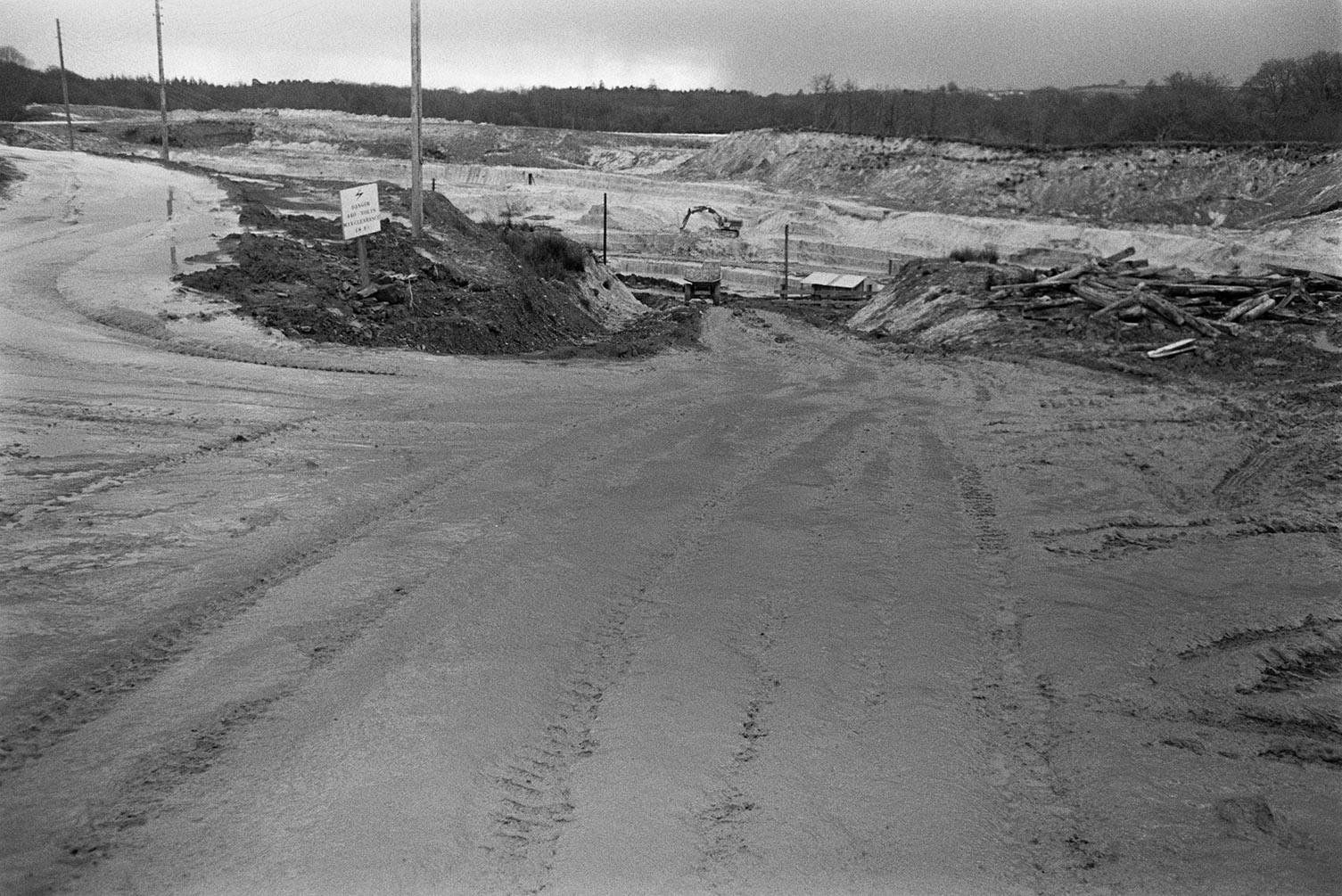 Clay works with a digger excavating in the background at North Devon Clay Pit, Meeth. A road down to the quarry and timber is visible in the foreground.