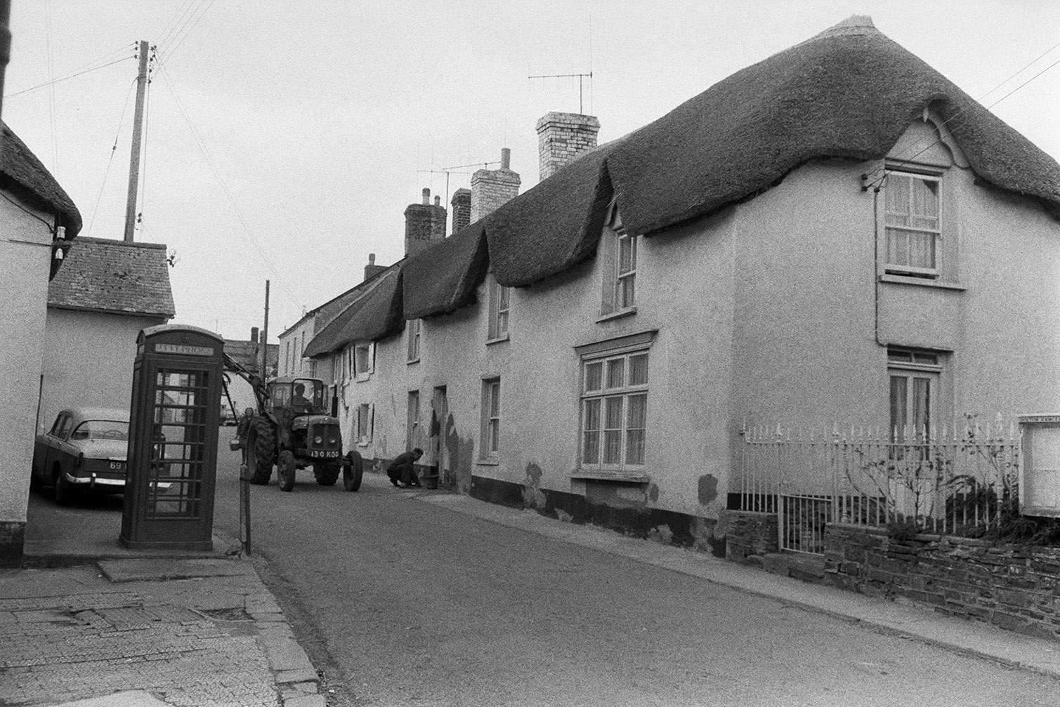 A tractor driving down Fore Street, Dolton. Thatched cottages and a telephone box are visible in the street.