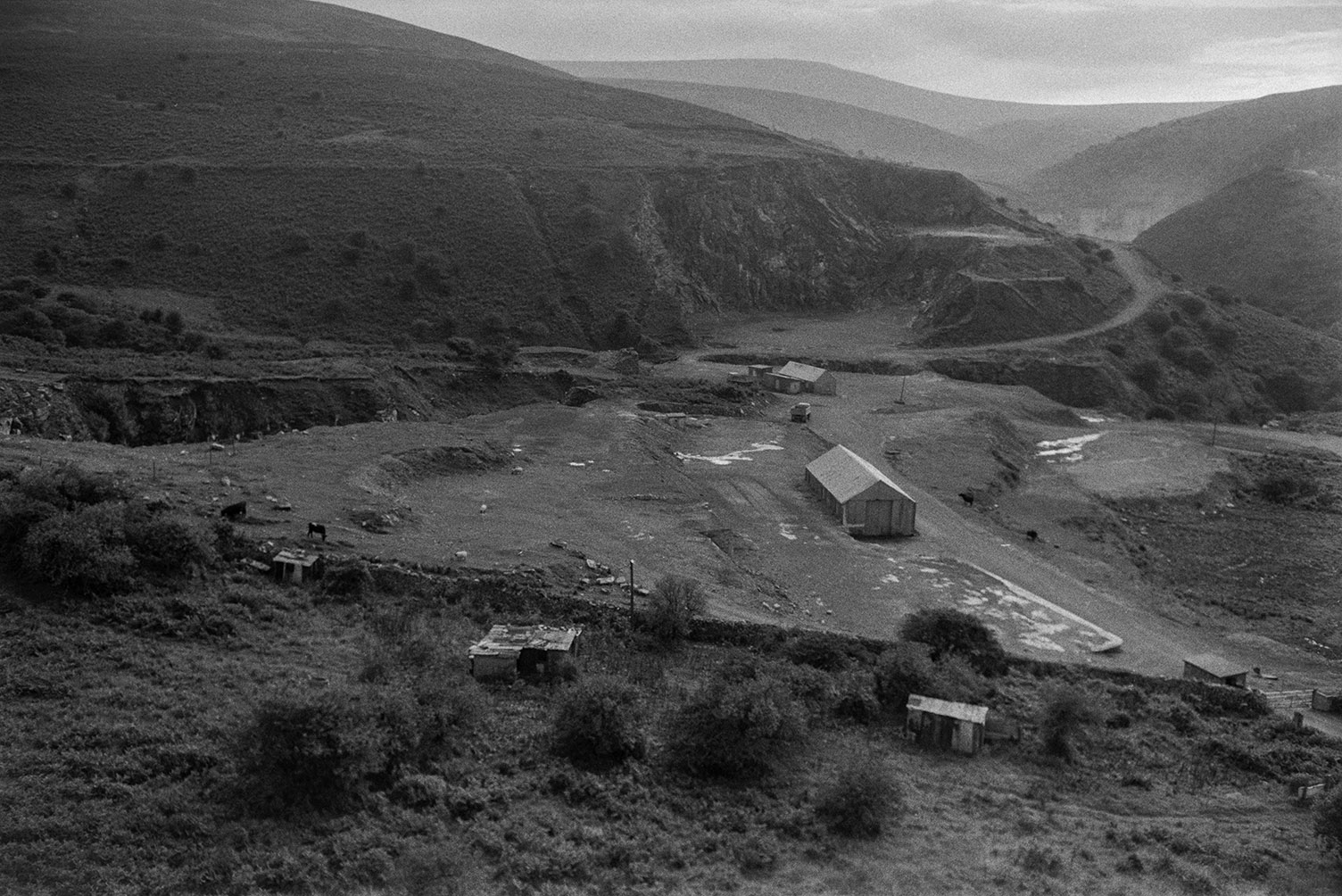 A quarry on a hillside with buildings and sheds in the foreground. It is possibly Merrivale Quarry.