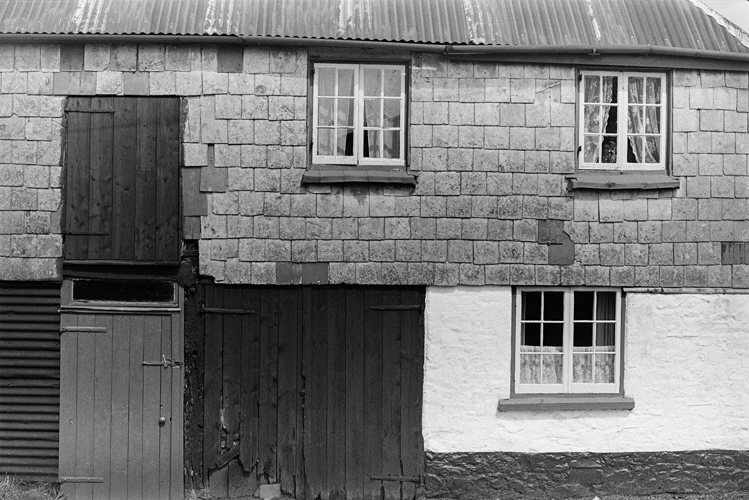 A slate clad cottage with large wooden doors at Rackenford. It also has a corrugated iron roof.