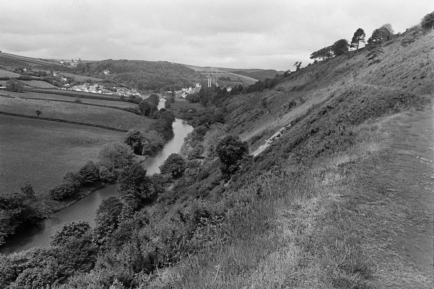 A view of the River Torridge running along the bottom of a valley and a village in the distance. The image is taken from Torrington.