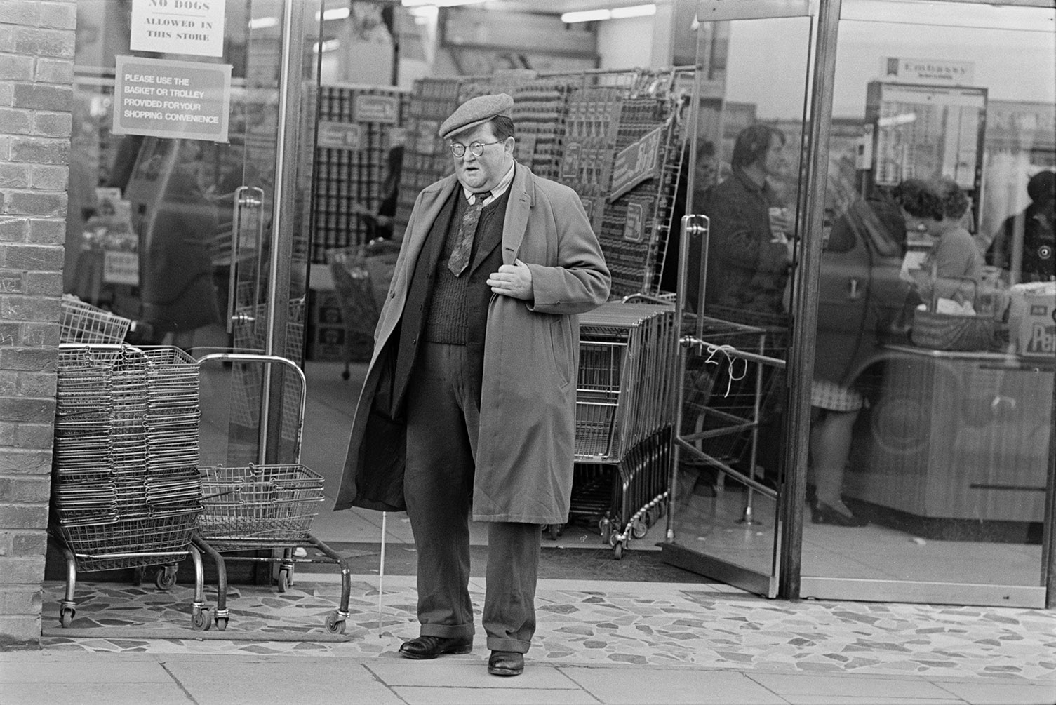 A man leaving a supermarket in Barnstaple. Shopping baskets are stacked outside the shop front.