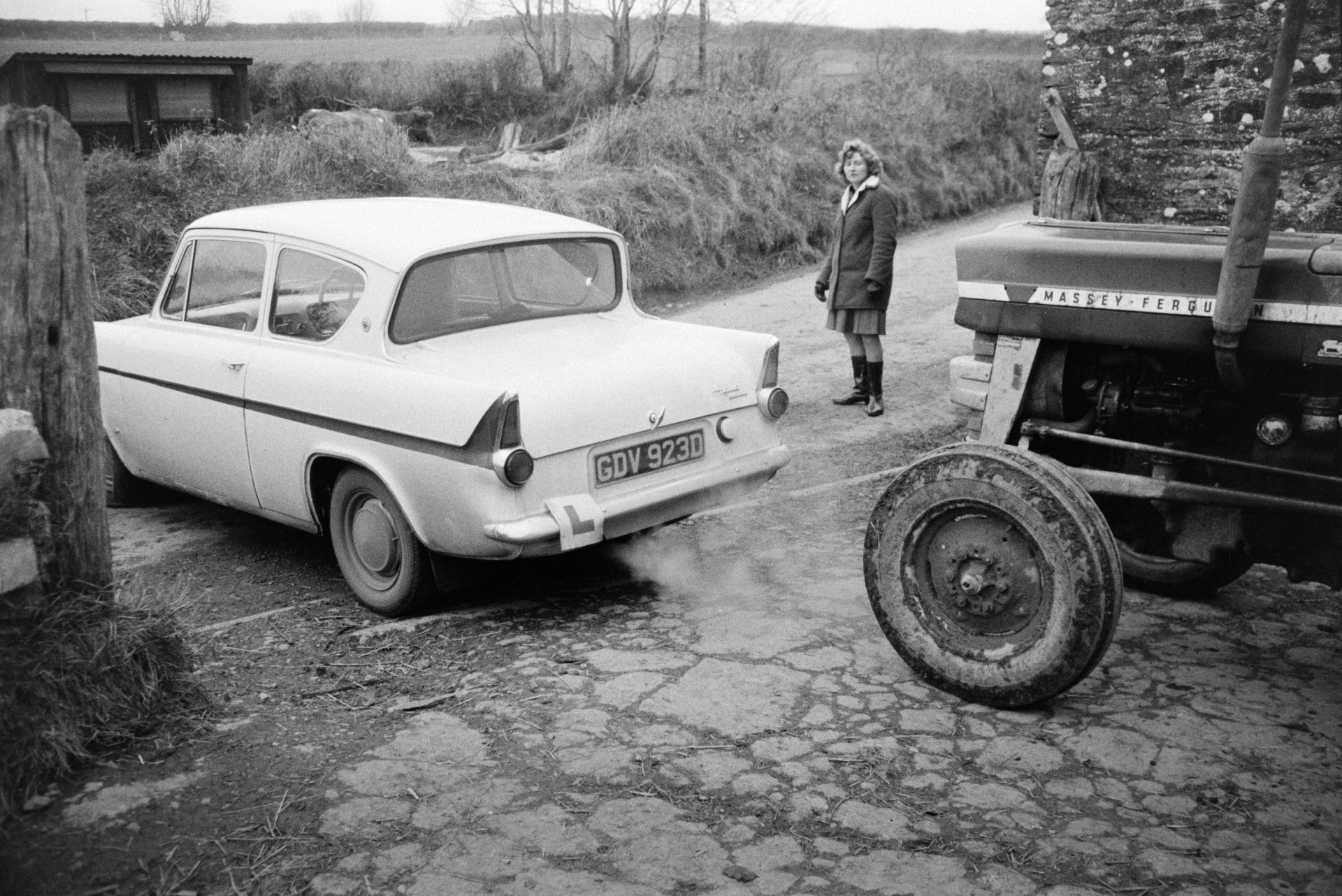 Derek Bright starting Marylin Bourne's car as she watches, at Mill Road Farm, Beaford. A Massey Fergusson tractor is behind the car. The farm was also known as Jeffrys.
