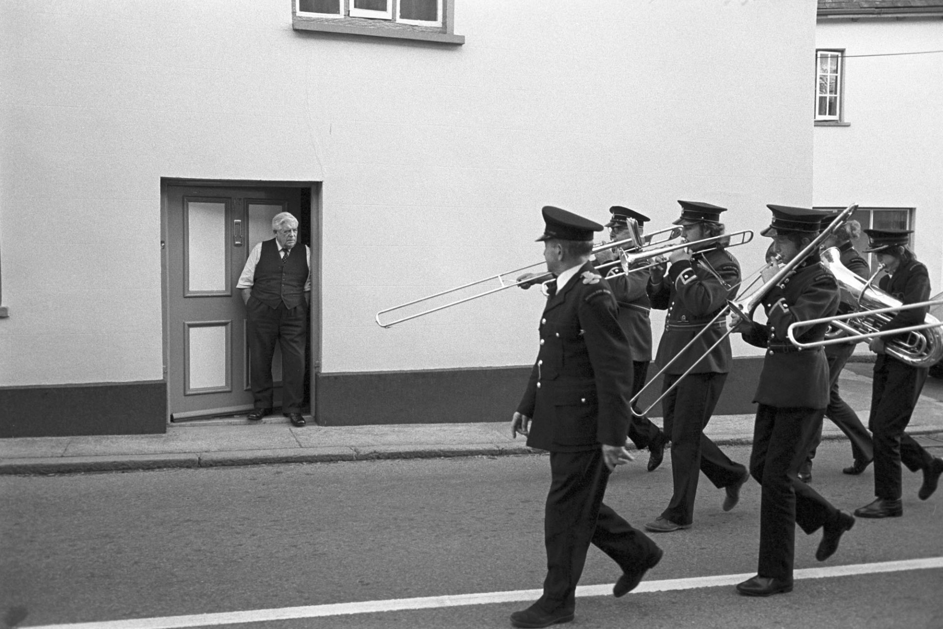 Hatherleigh Silver Band leading British & Foreign Bible Society Parade.
[A man is watching Hatherleigh Silver Band parade past from his front door at Hatherleigh in the British & Foreign Bible Soicety Parade.]