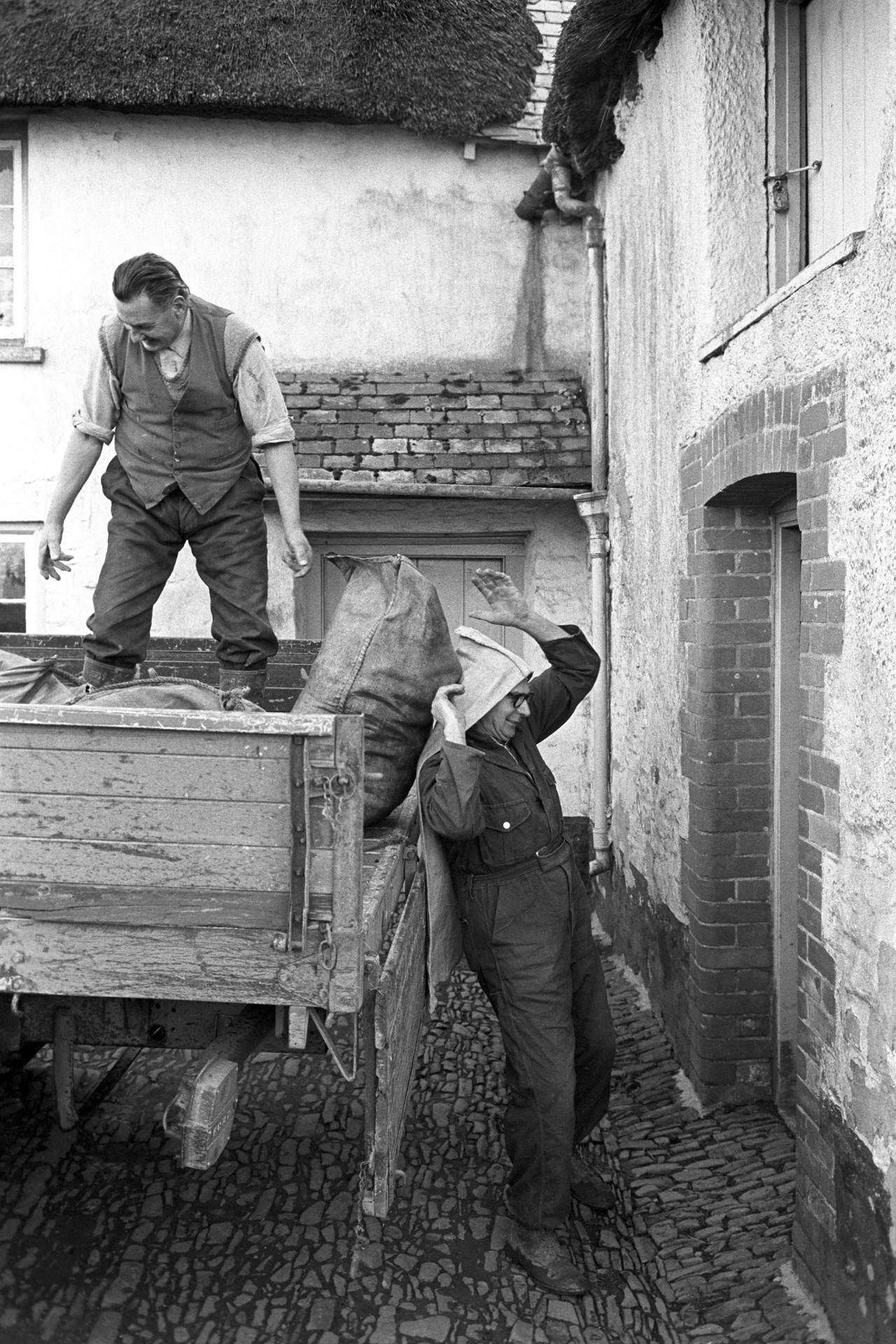 Delivering coal to farm.
[Two men from J Coal & Sons, coal merchants, unloading sacks of coal from a lorry and taking them into the farmhouse at Elliots, Roborough.]