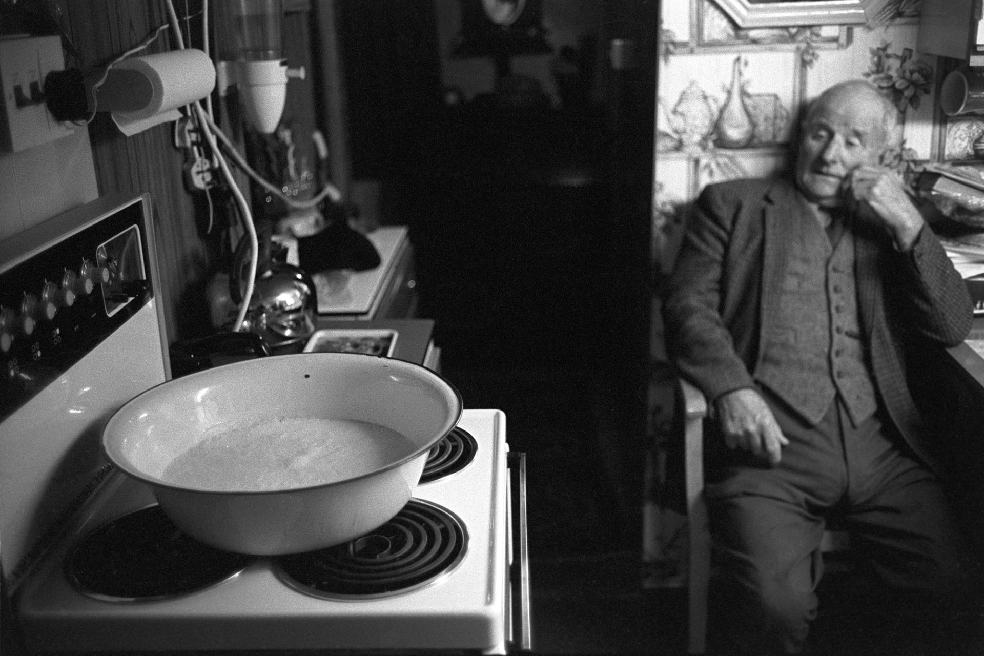 Clotted cream on stove, old man in background.
[George Voysey sat in his kitchen looking at a bowl of clotted cream on the cooker, at Cawseys, Roborough.]