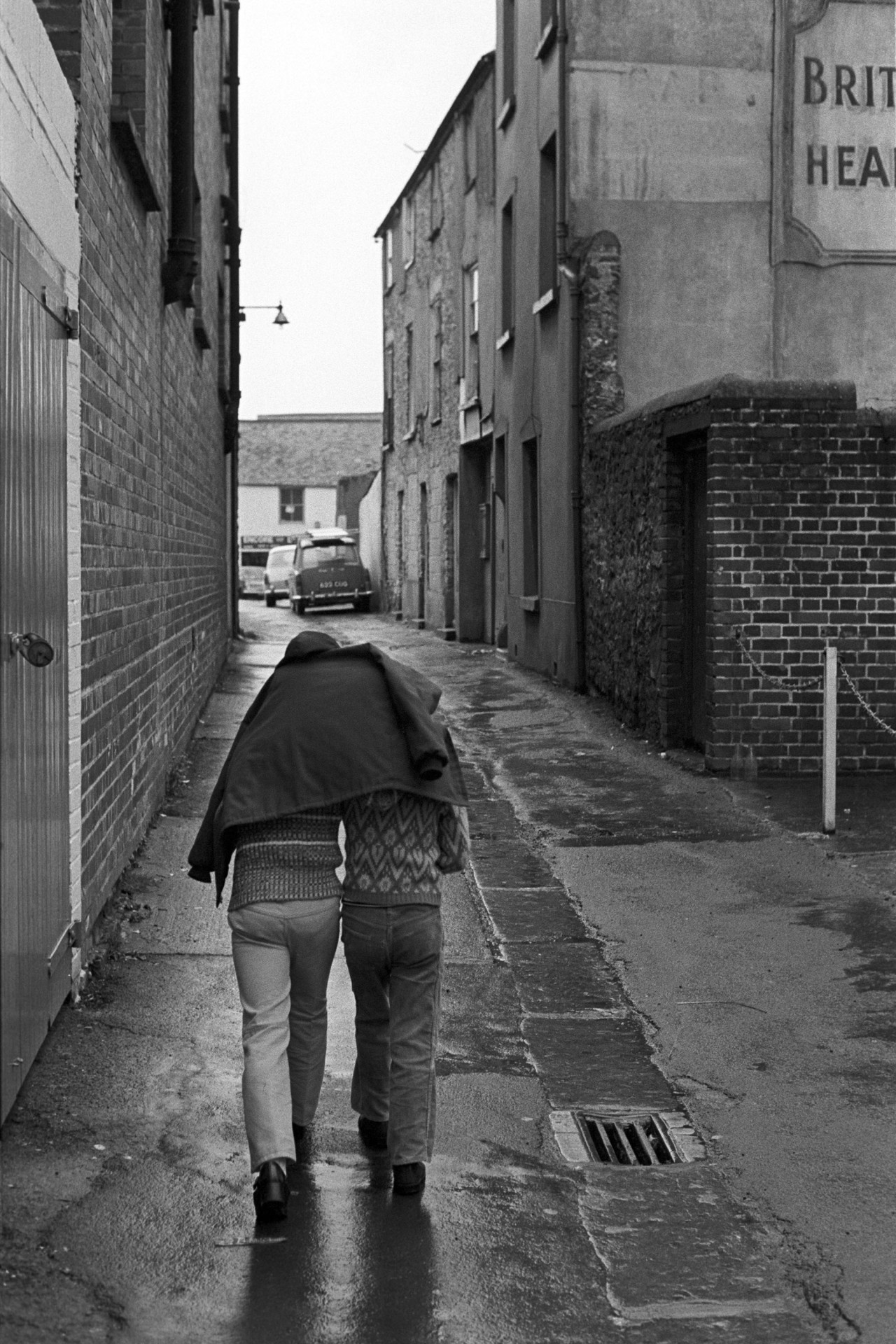 Backstreet with two children.
[Two people walking along a backstreet, huddled under a coat, in Bideford.]