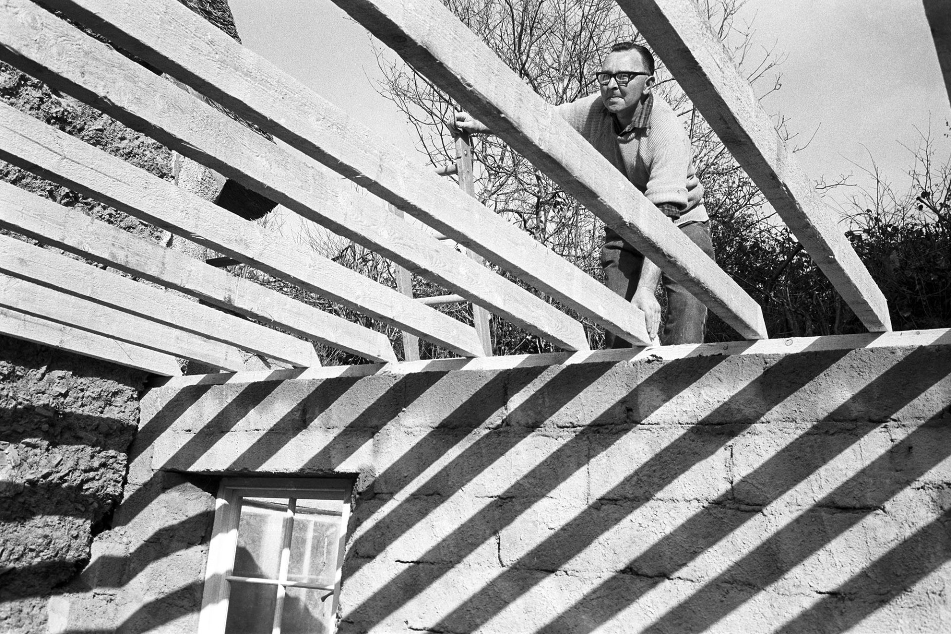 Man fixing beams in new extension to cottage.
[Clifford Palmer fixing roof timbers on an extension to the Ravilious' thatched cottage at Addisford, Dolton. See the 'Additional notes by James Ravilious' field for more information.]