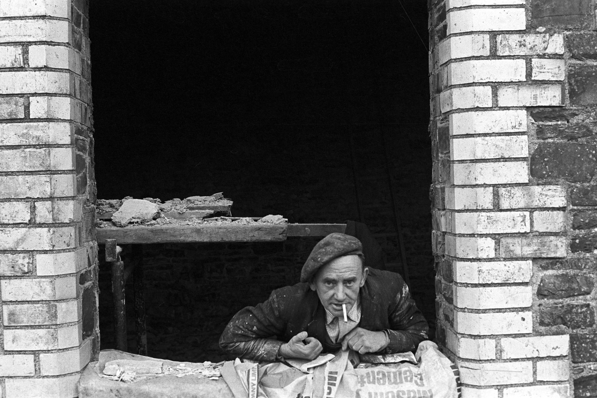 Builder with cigarette looking out of window.
[Argo Pickard smoking a cigarette and looking out of a window in a building he's converting from a stable into a house at Barlands, Dolton.]