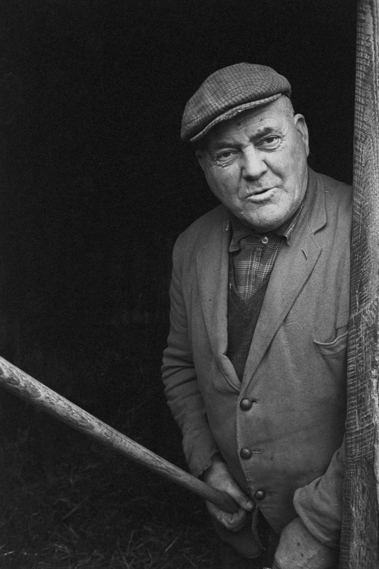Farmer with stick at shed door. 
[Cyril Bennett leaning against a door frame, holding a stick, at Cuppers Piece, Beaford.]