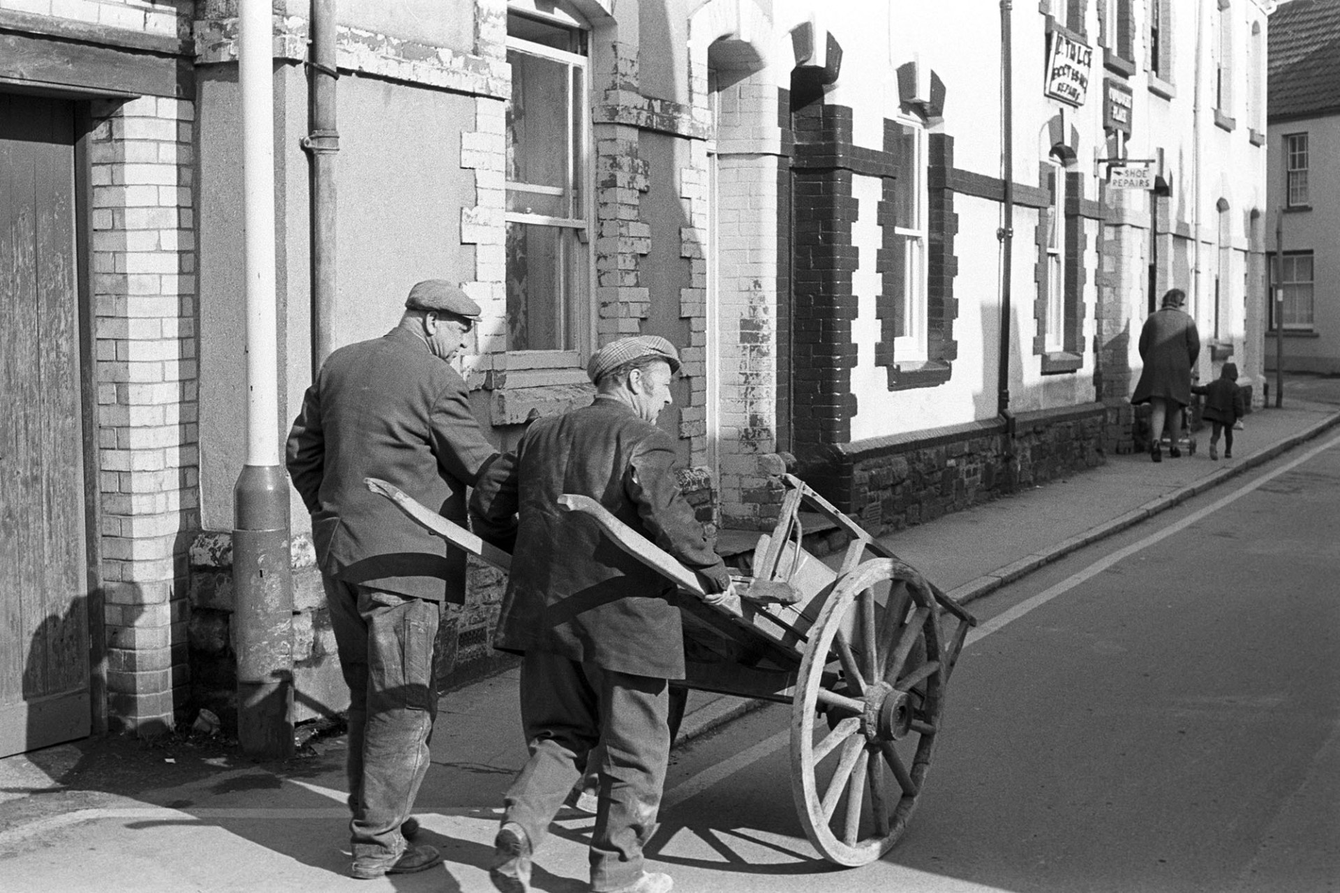 Two men with hand cart, presumably builders. 
[Two men pushing a wooden hand cart down Silver Street, Barnstaple.]