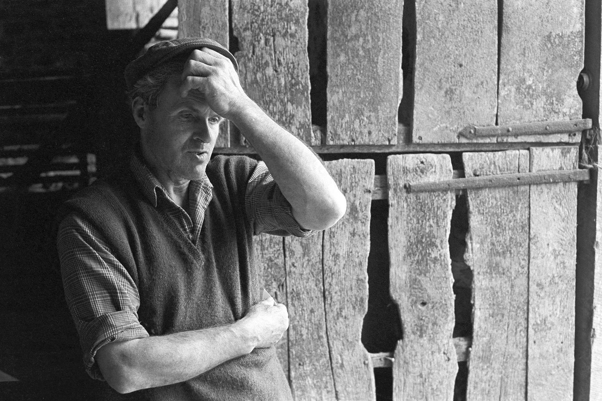 Portrait of farmer against barn door. 
[Alf Pugsley leaning against a wooden barn door at Lower Langham, Dolton.]