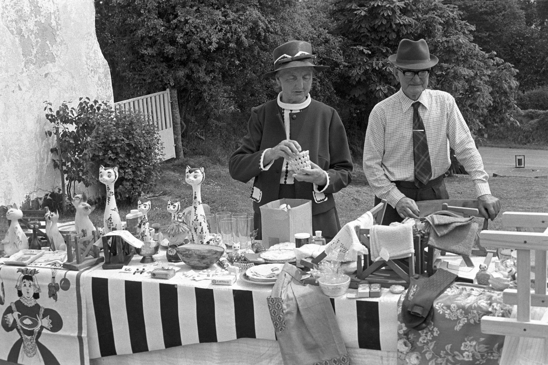 Church Fete jumble stall, couple arranging goods. 
[A couple arranging a bric-a-brac stall at Iddesleigh Church Fete.]