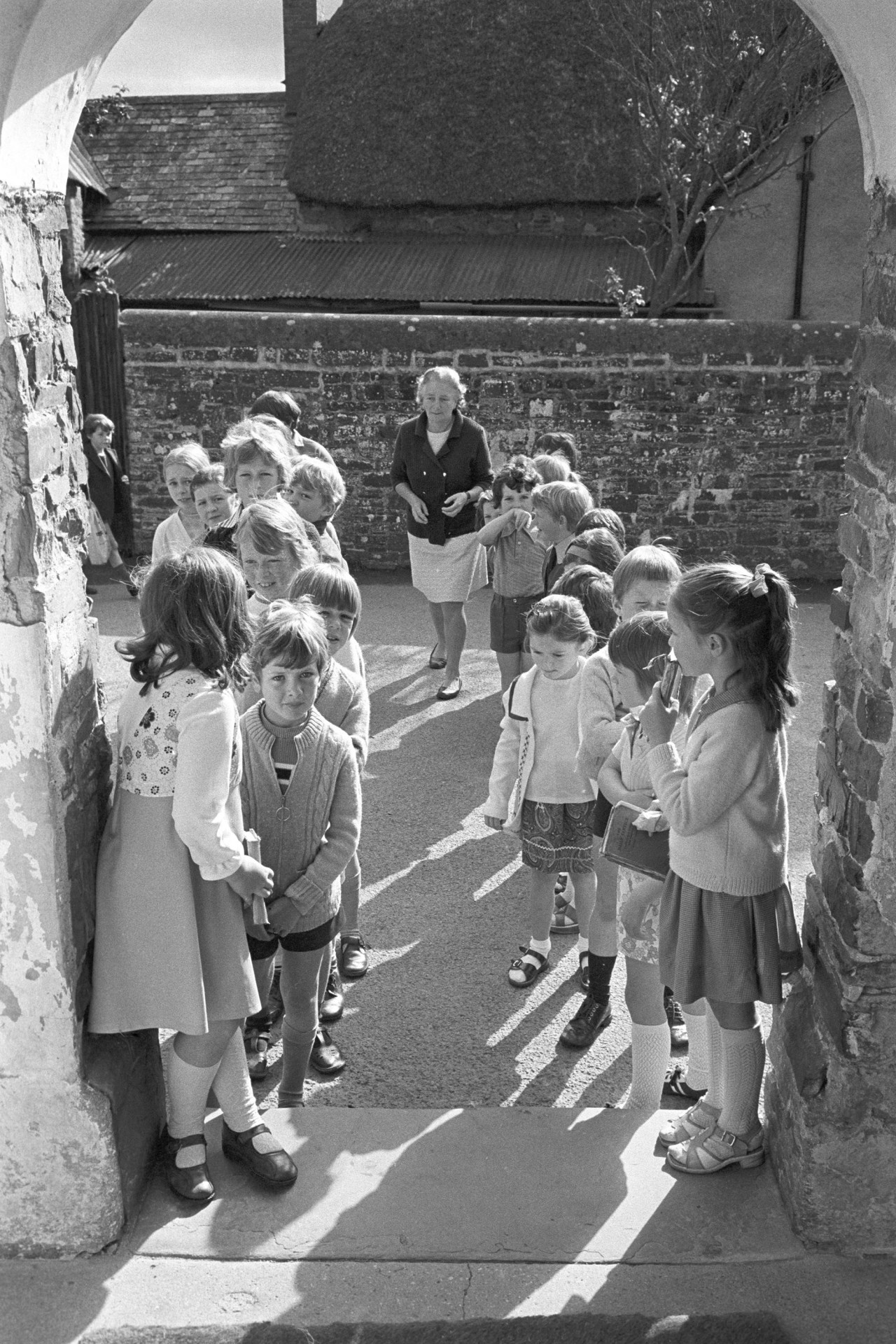 Primary School children lining up in yard before going in to school. 
[Schoolchildren lining up in the playground, waiting to go into Dolton Primary School. Mrs Gough, a teacher, is walking between the lines of children.]